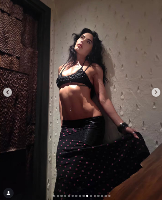 Posando contra una pared texturizada en un ambiente cálido e íntimo, Emilia Attias deslumbró con un conjunto de dos piezas compuesto por un diminuto top negro de tirantes finos con detalles texturizados y una falda larga de tiro bajo en tono oscuro estampada con lunares claros. La artista dejó al descubierto su tonificado abdomen mientras sostenía el vuelo de la prenda. | Fuente: Instagram/emilia_att