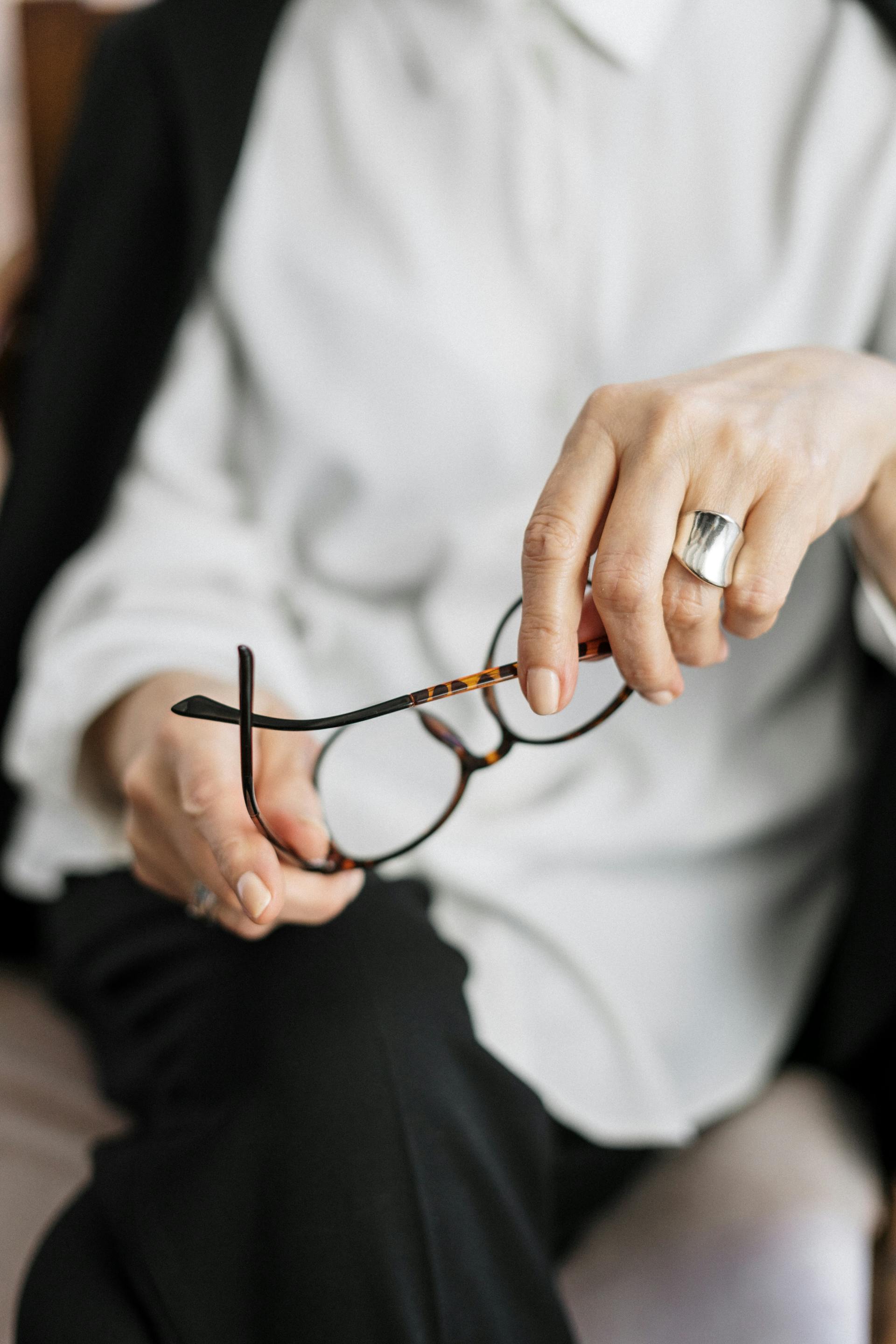 Una terapeuta sujetando sus gafas de montura marrón | Fuente: Pexels