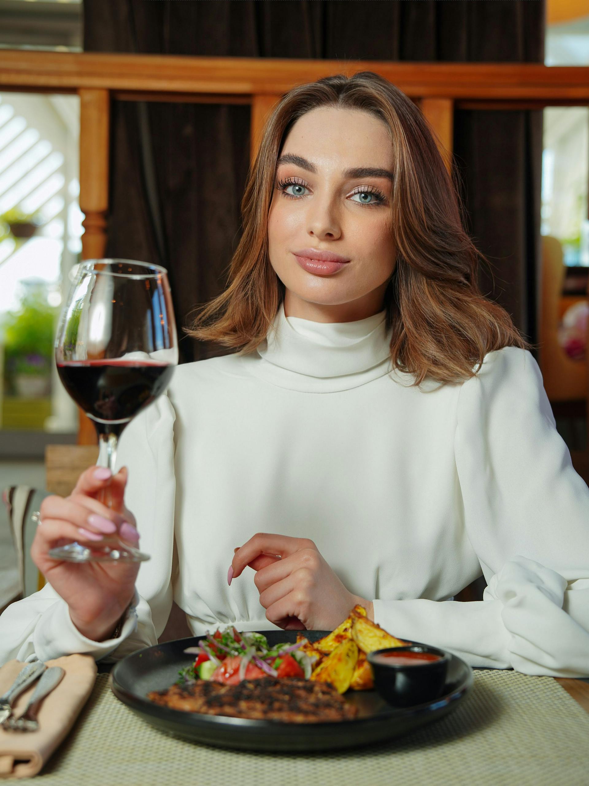 Una mujer sentada a la mesa sosteniendo un vaso de vino tinto | Fuente: Pexels