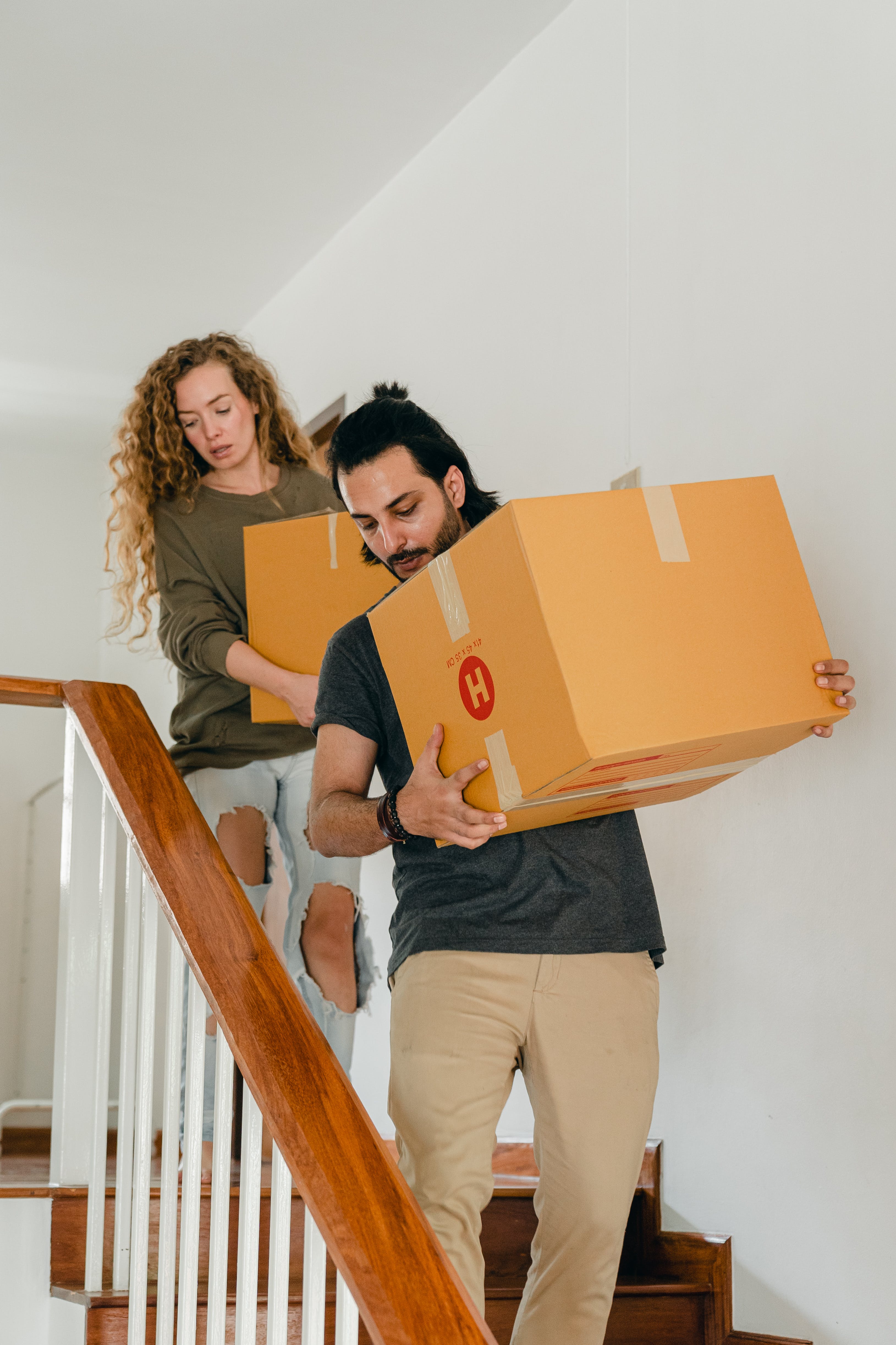 Una joven pareja cargando cajas mientras baja las escaleras | Foto: Pexels