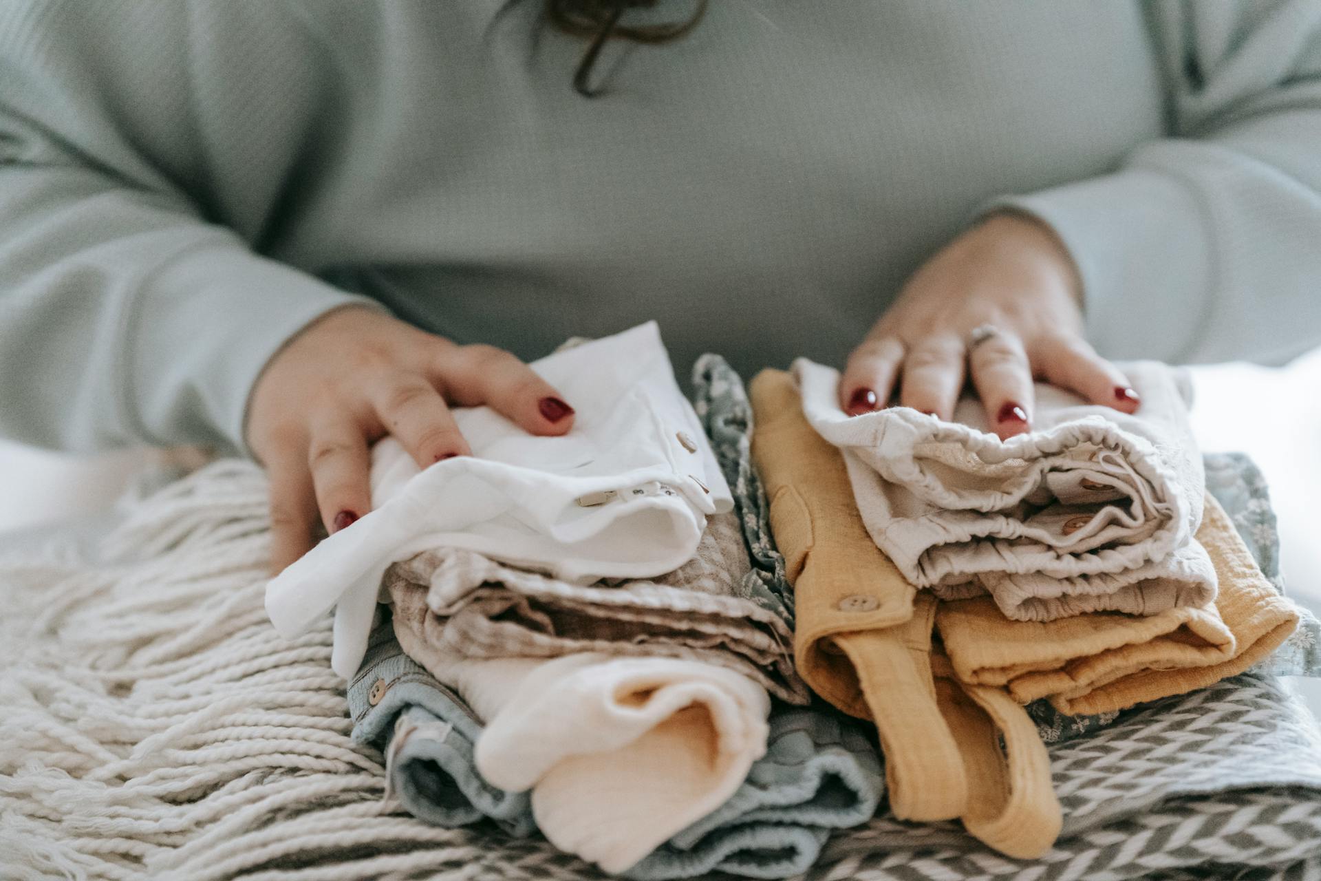 Una mujer con ropa de bebé doblada | Fuente: Pexels