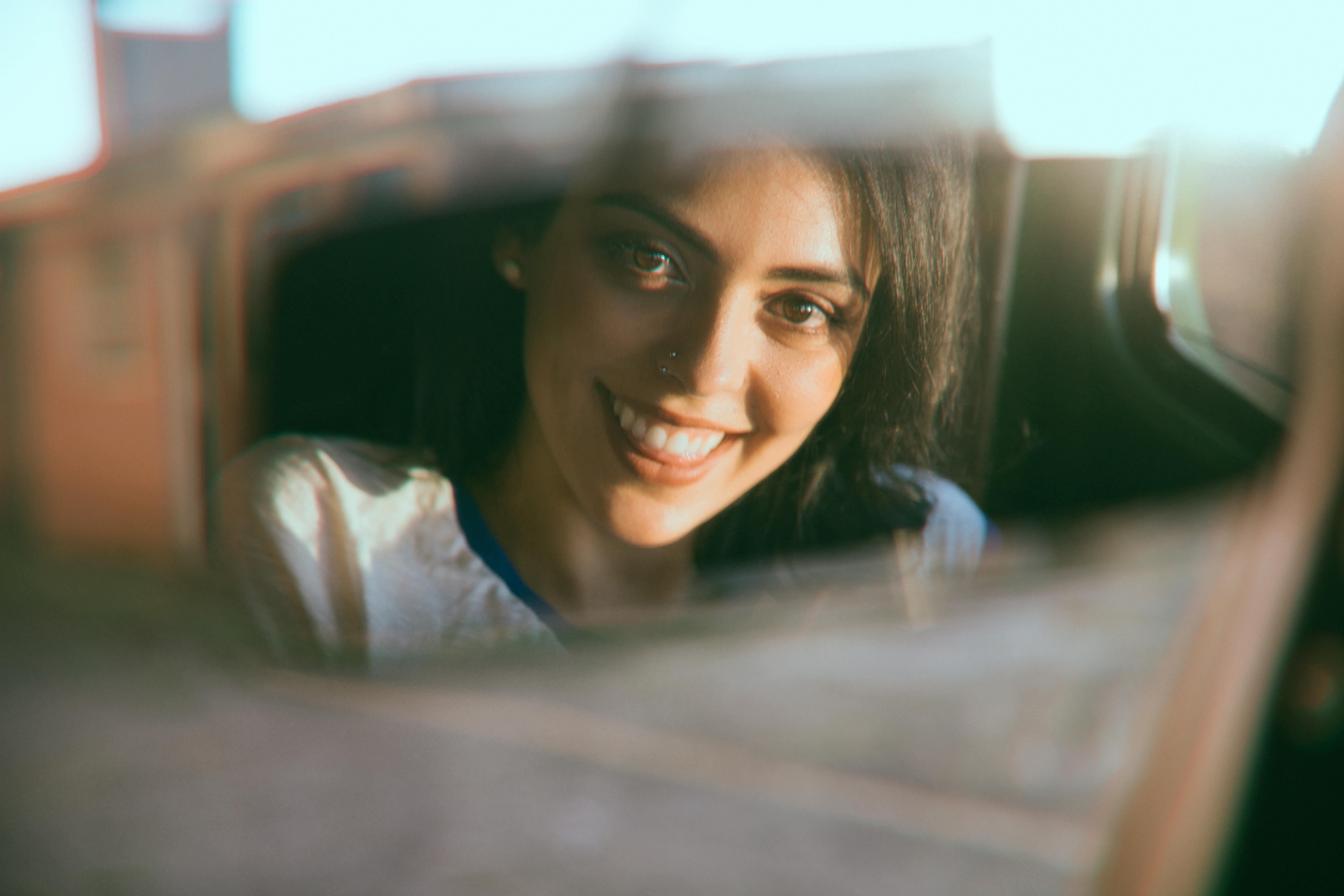 Una mujer feliz mirando por el retrovisor mientras conduce | Fuente: Pexels