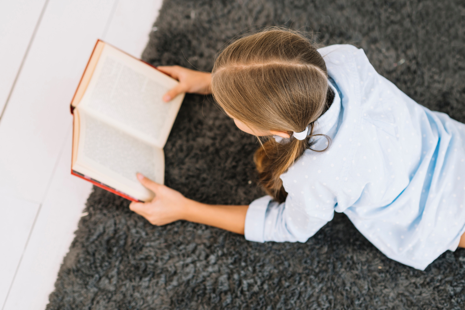 Una chica tumbada en una alfombra y leyendo un libro | Fuente: Freepik