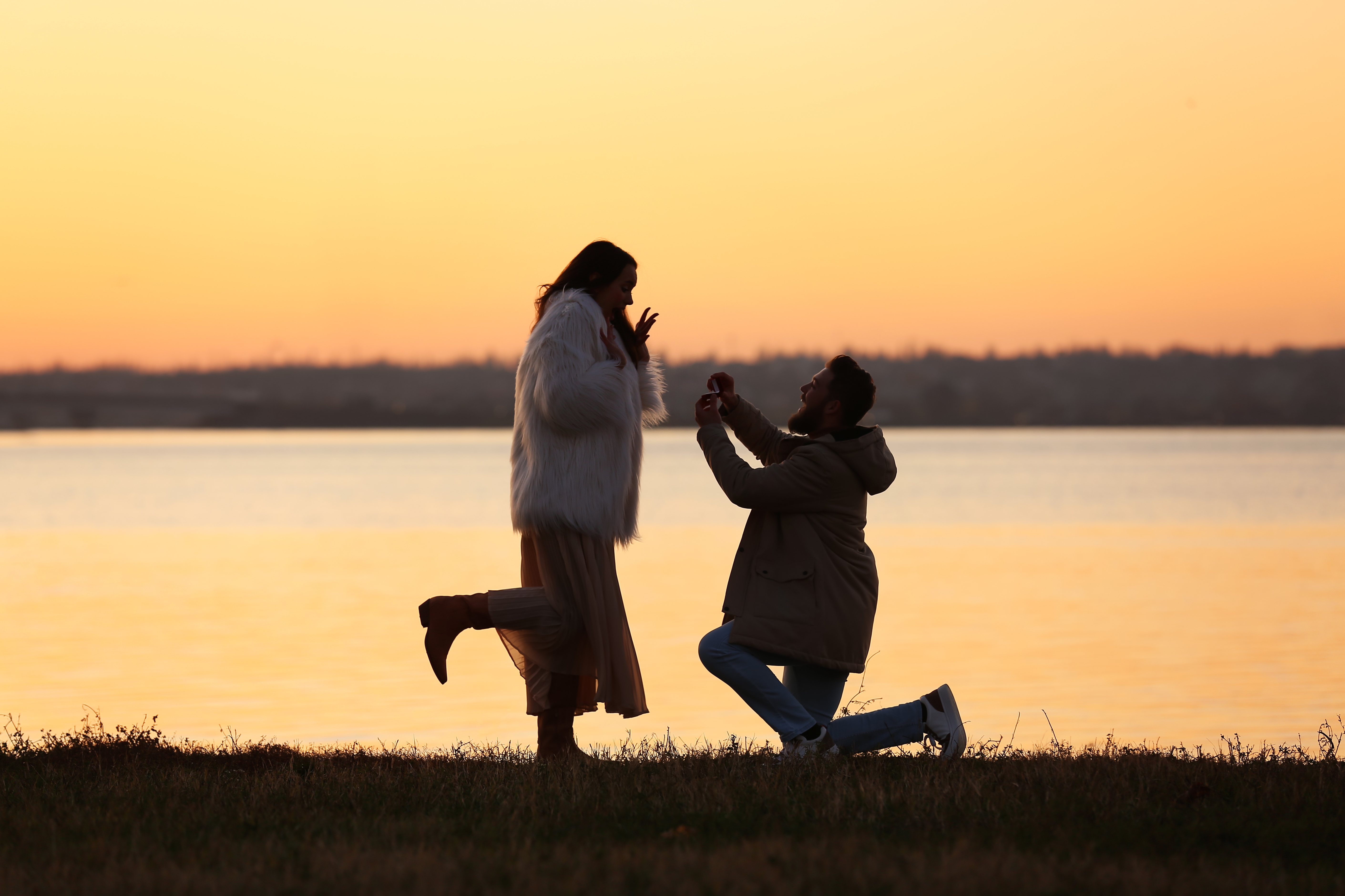 Joven pidiéndole matrimonio a su novia cerca del río al atardecer. | Fuente: Shutterstock