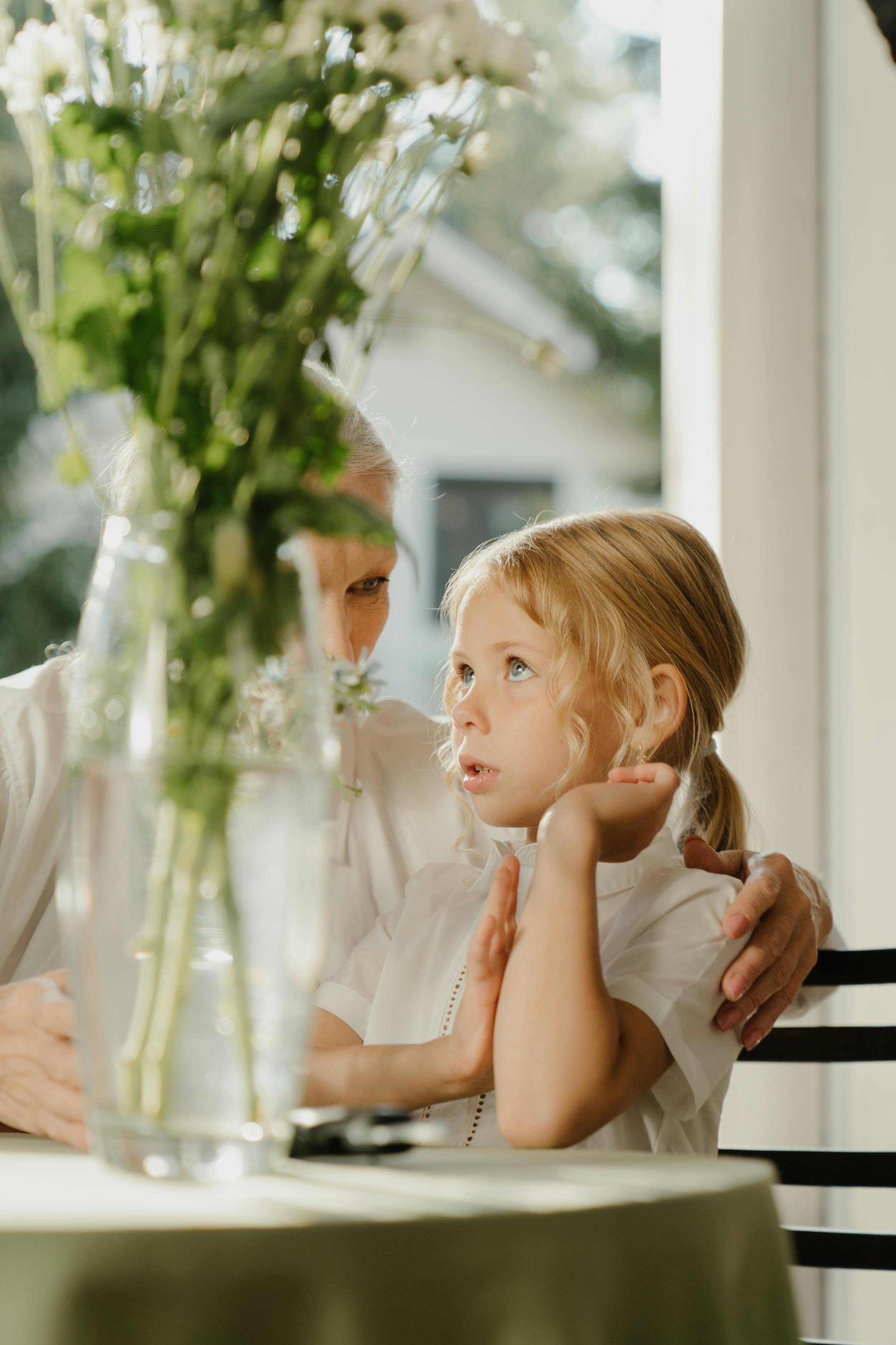 Una mujer mayor y una niña junto a un jarrón de flores sobre una mesa | Fuente: Pexels