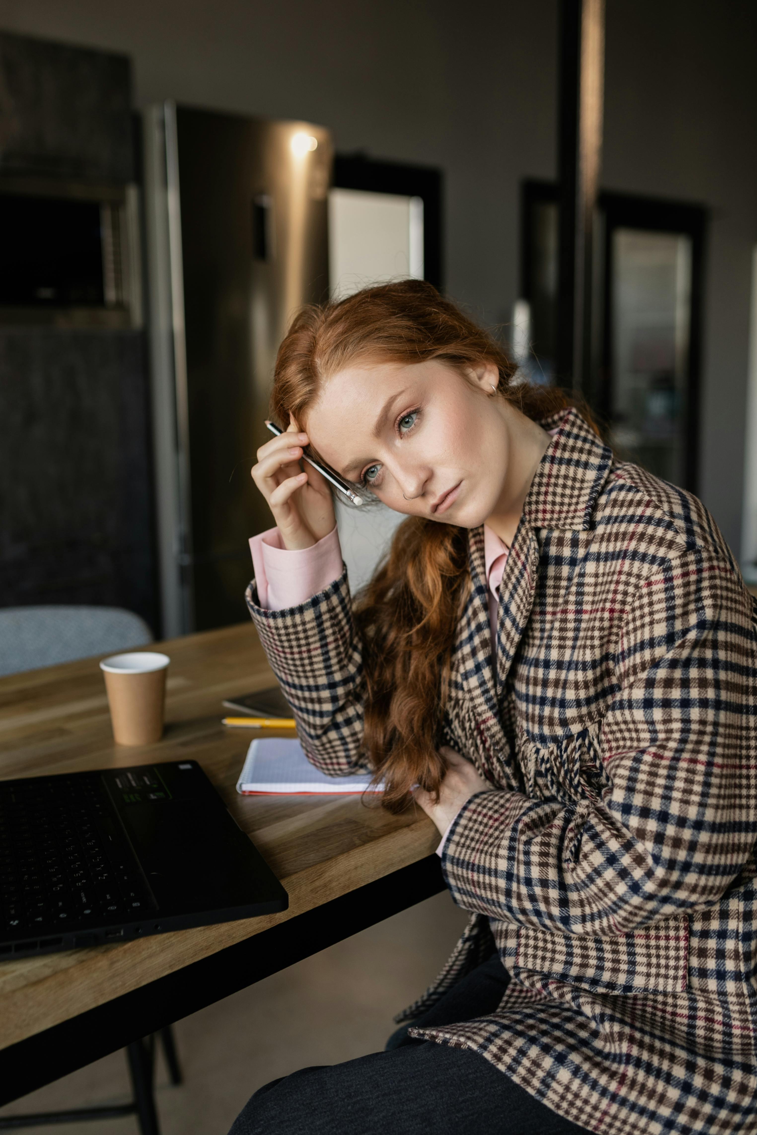 Una mujer preocupada con traje marrón sentada en una mesa | Fuente: Pexels