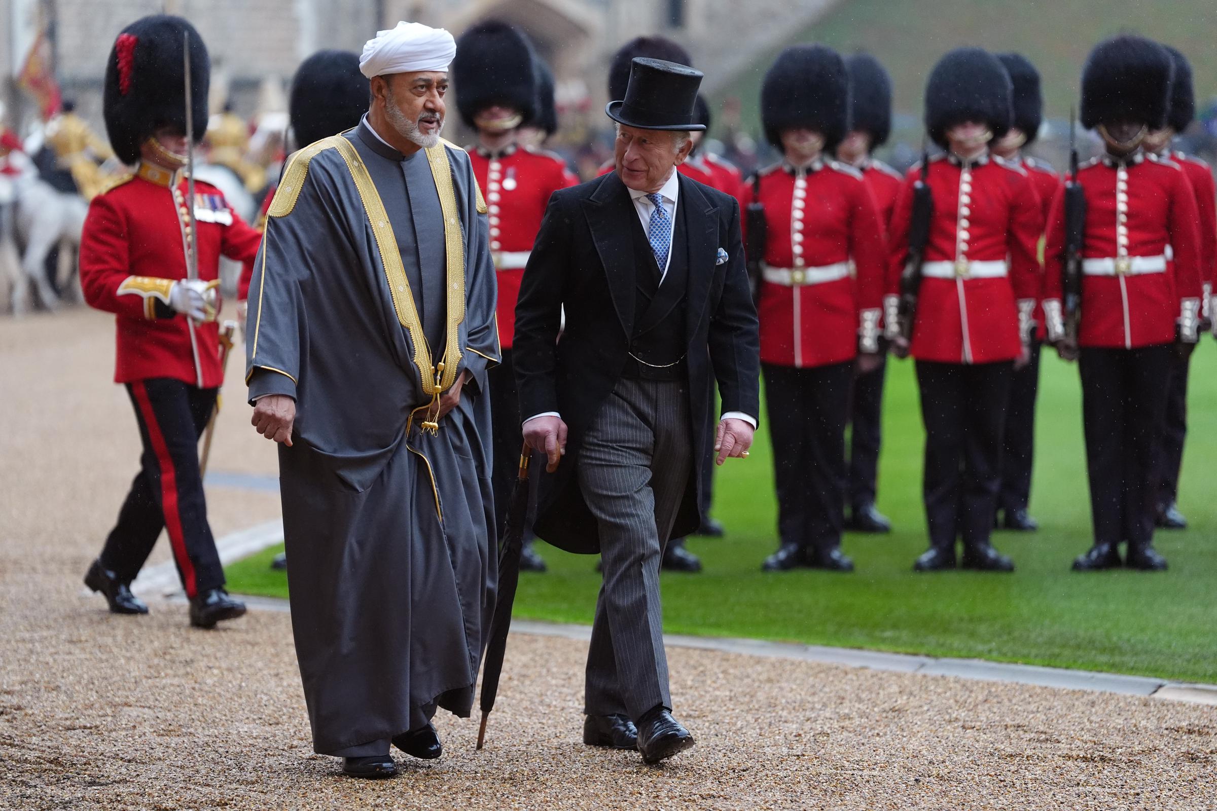 El rey Charles III y el sultán Haitham bin Tarik de Omán inspeccionan la guardia militar durante la bienvenida oficial en el castillo de Windsor, Inglaterra, el 20 de octubre de 2026. Detrás, los guardias forman con túnicas rojas y altos gorros de piel. Charles III viste chaqué negro, pantalones a rayas y sombrero de copa de seda, y lleva un paraguas mientras camina junto al sultán, vestido con un bisht gris tradicional con bordados dorados y turbante blanco. | Fuente: Getty Images