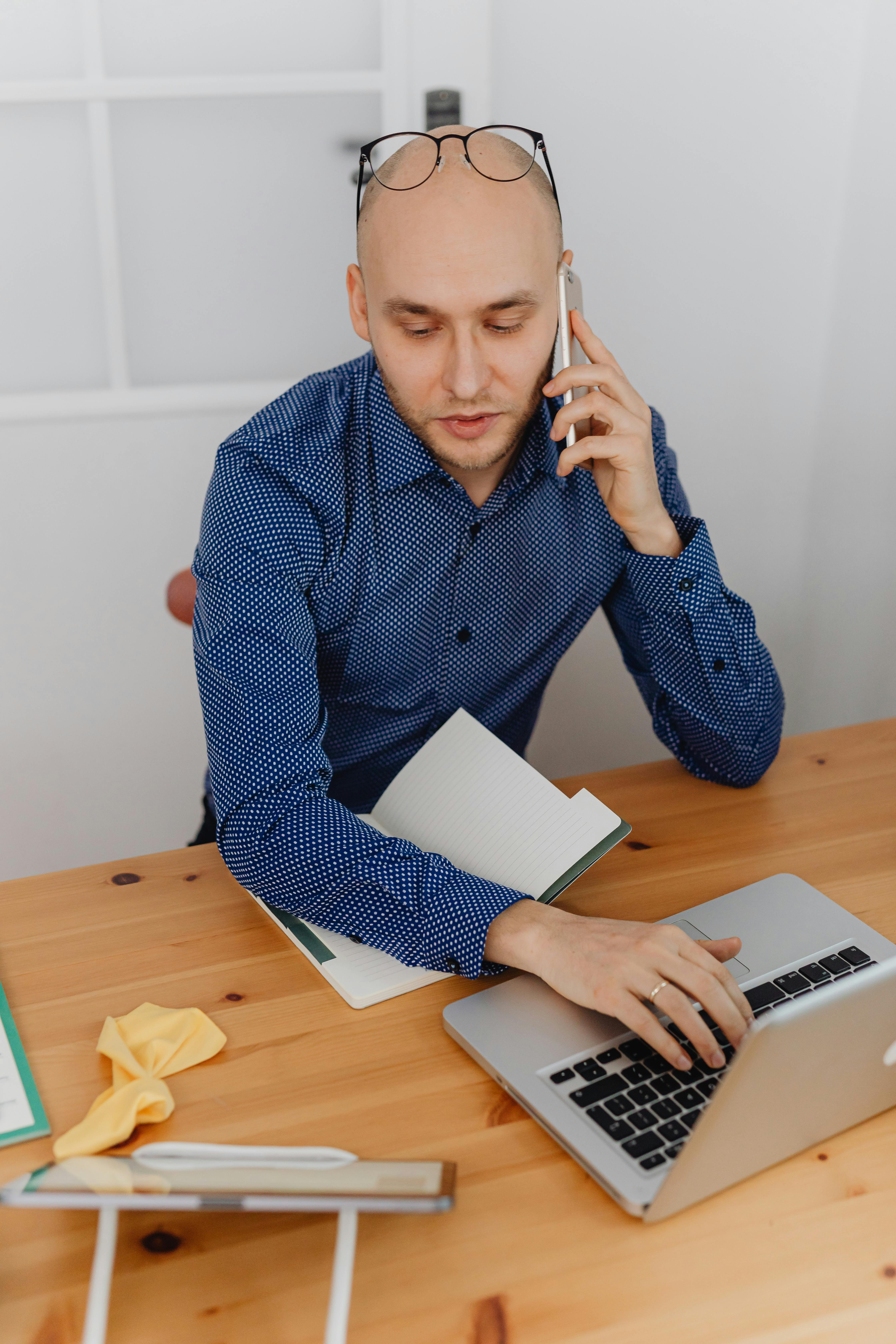 Un hombre hablando por teléfono mientras trabaja con un portátil | Foto: Pexels