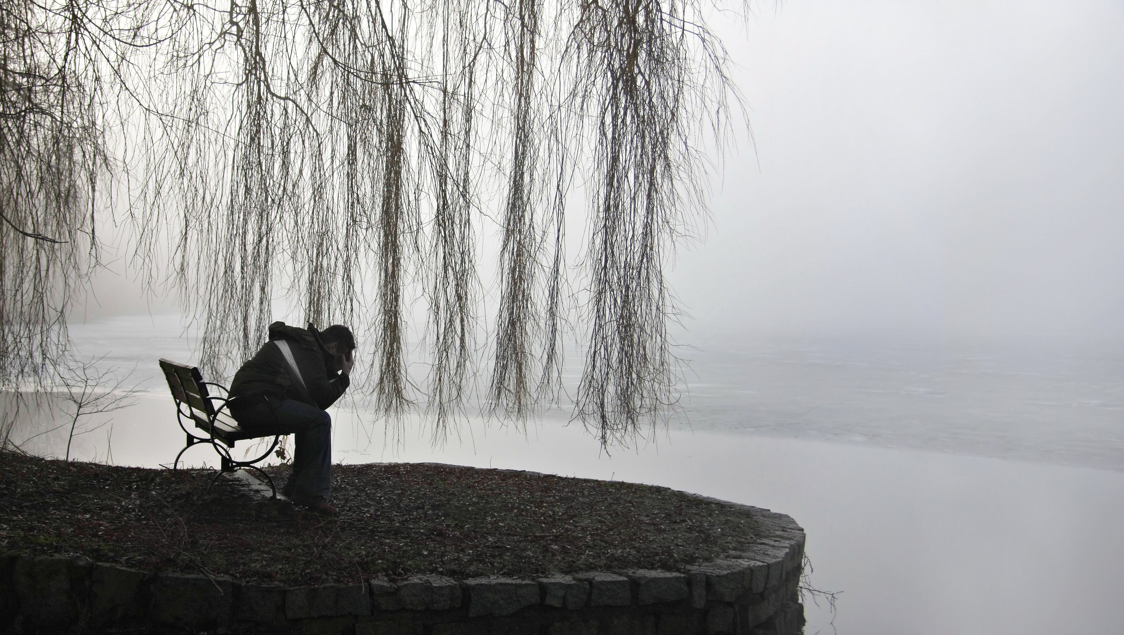 Hombre con su rostro entre sus manos, sentado frente a un lago. | Foto: Shutterstock