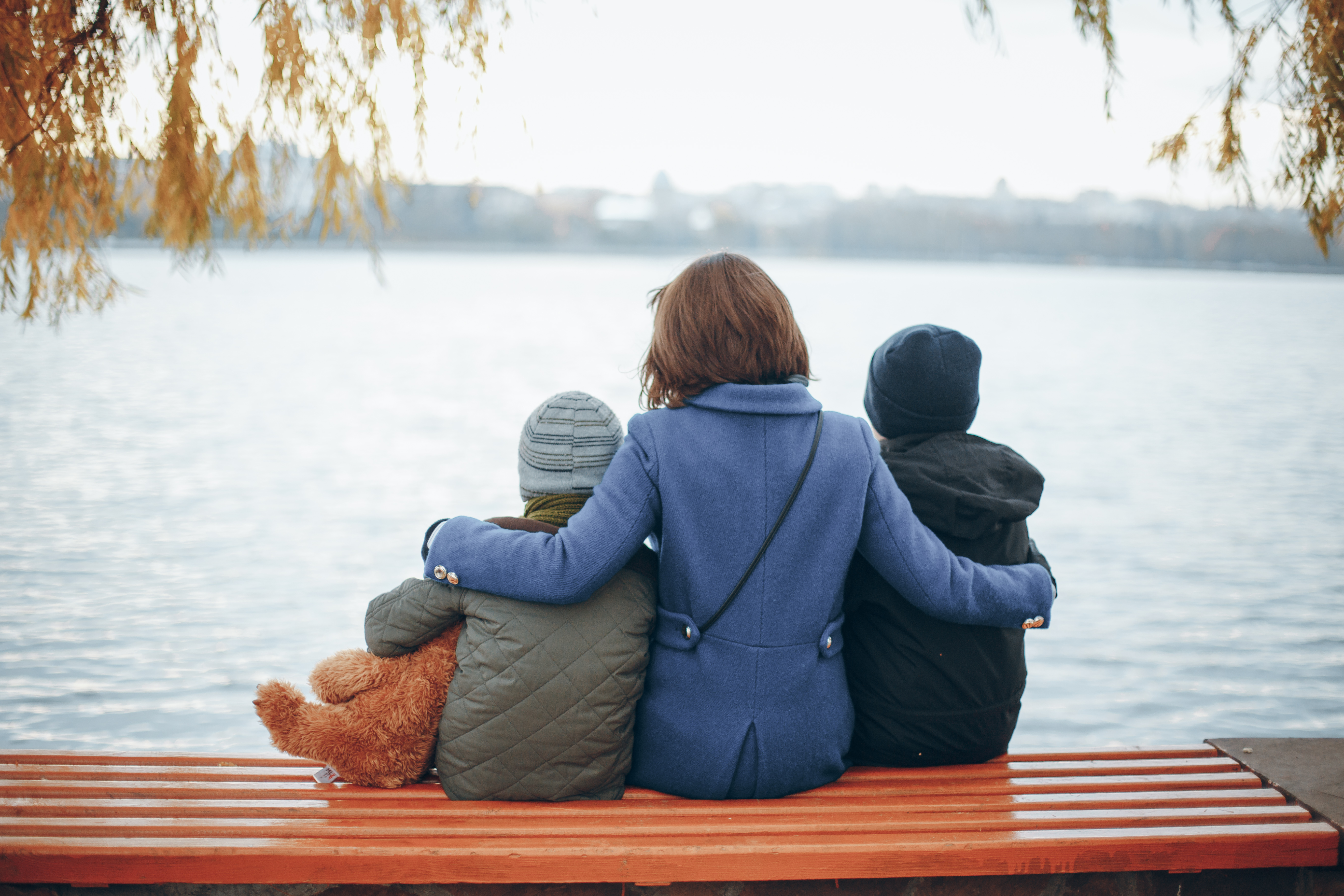 Una mujer sentada con sus dos hijos cerca del río | Foto: Shutterstock
