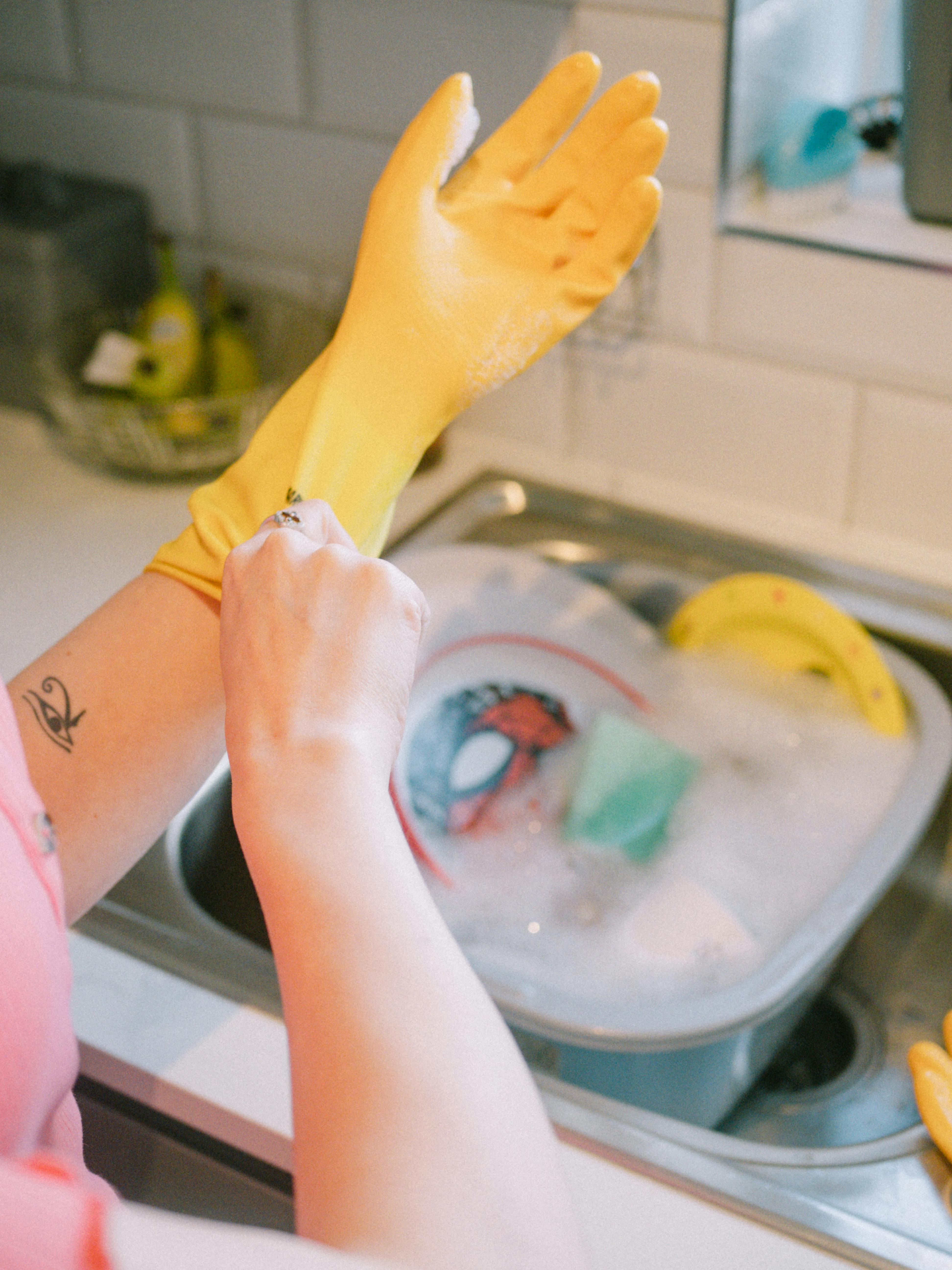 Una mujer con guantes preparada para lavar los platos | Fuente: Pexels