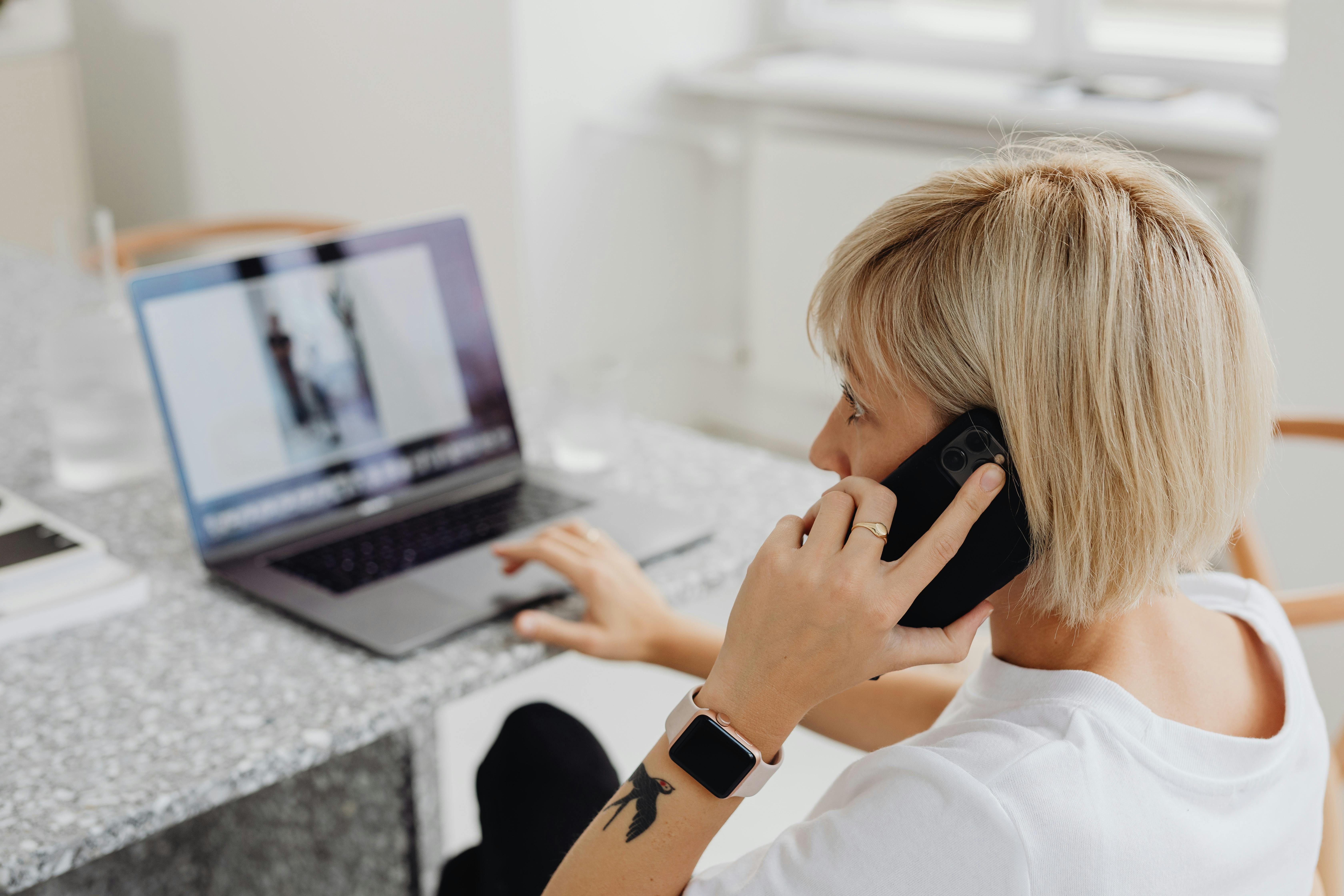 Una mujer utilizando un ordenador portátil mientras atiende una llamada telefónica | Fuente: Pexels