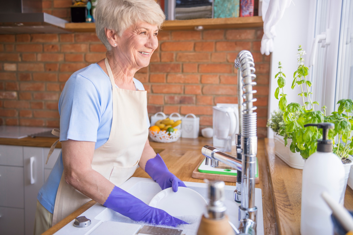 Una mujer mayor sonriente lavando los platos en la cocina | Fuente: Freepik