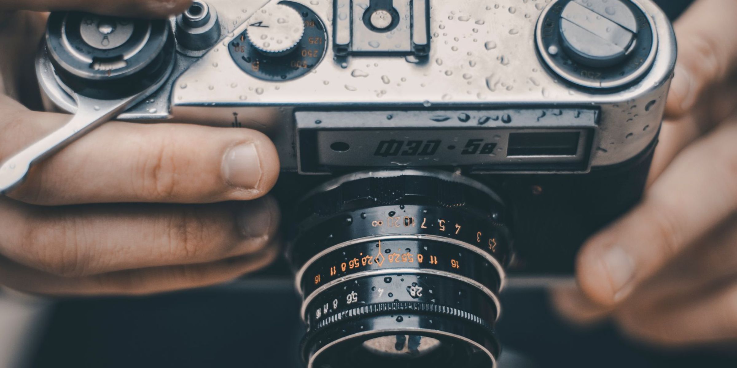 Un primer plano de unas manos que sostienen una cámara analógica antigua cubierta de gotas de agua | Fuente: Pexels