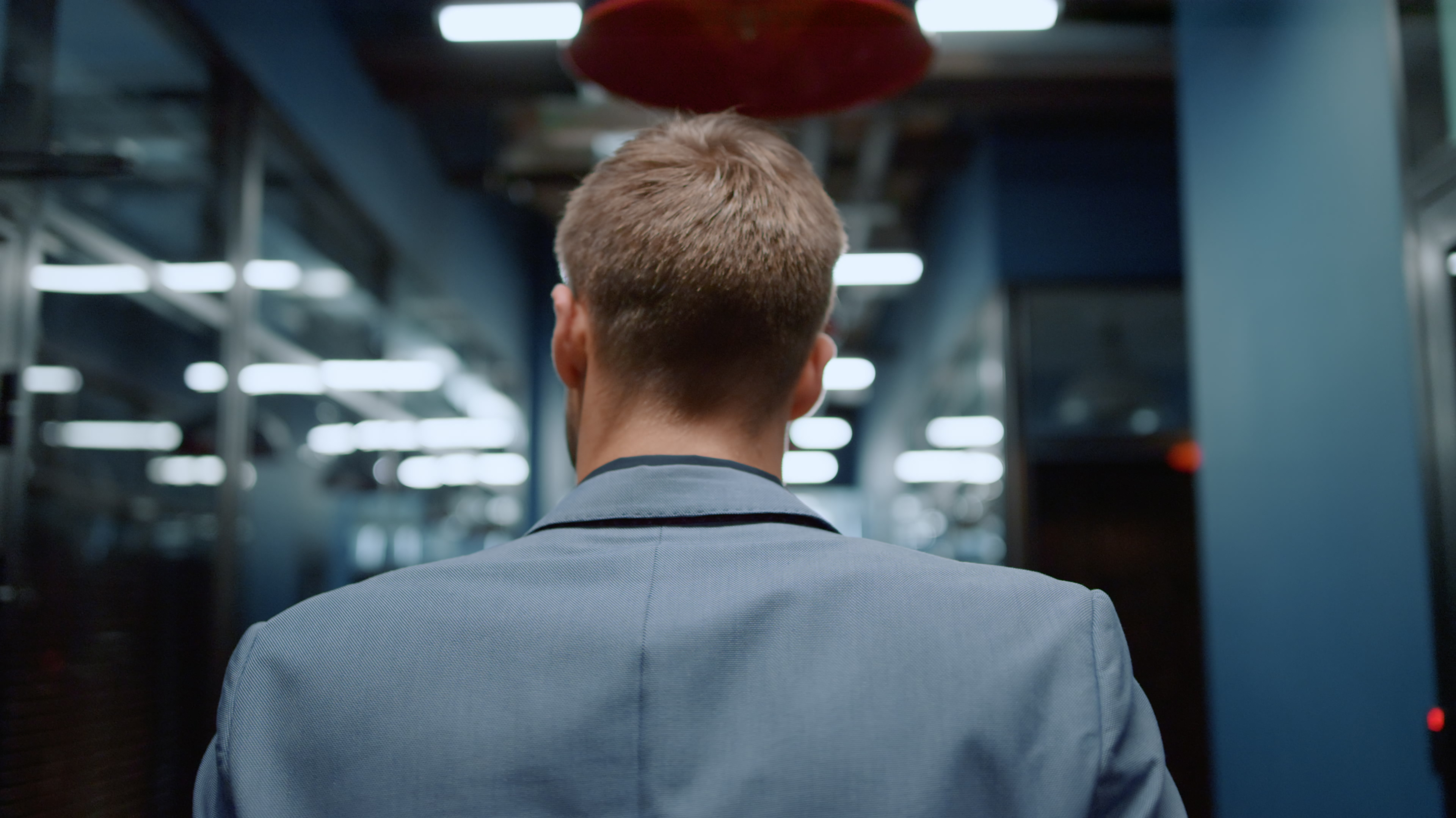 Vista trasera de hombre de negocios caminando con traje formal por un pasillo. | Fuente: Shutterstock