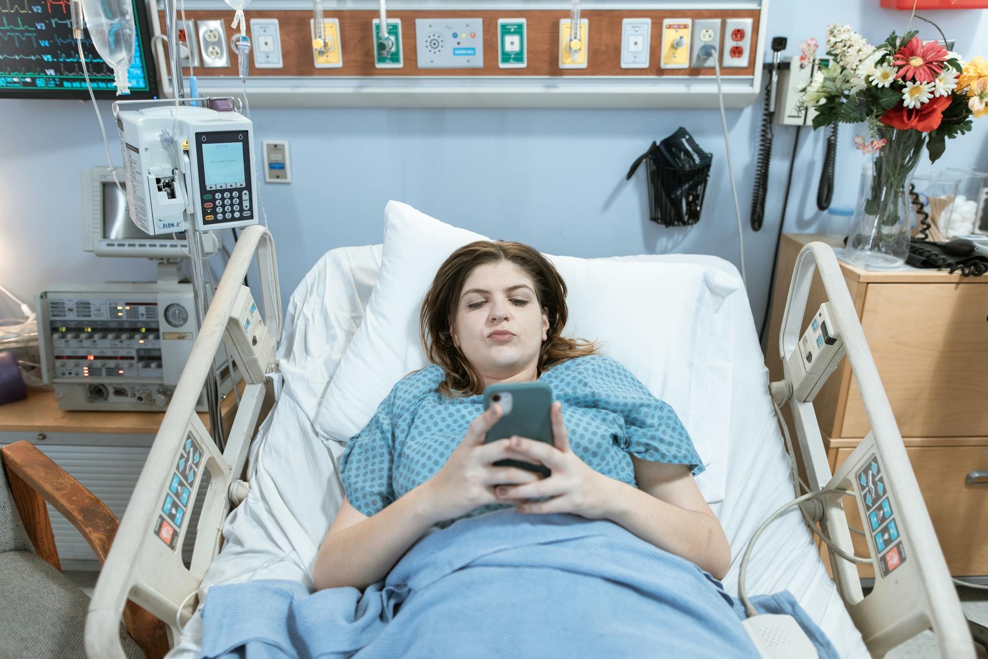 Una mujer mira su teléfono mientras está tumbada en la cama de un hospital | Fuente: Pexels