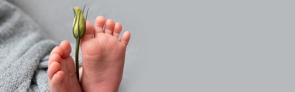 Pies de bebé recién nacido con una flor de eustoma. | Foto: Shutterstock.