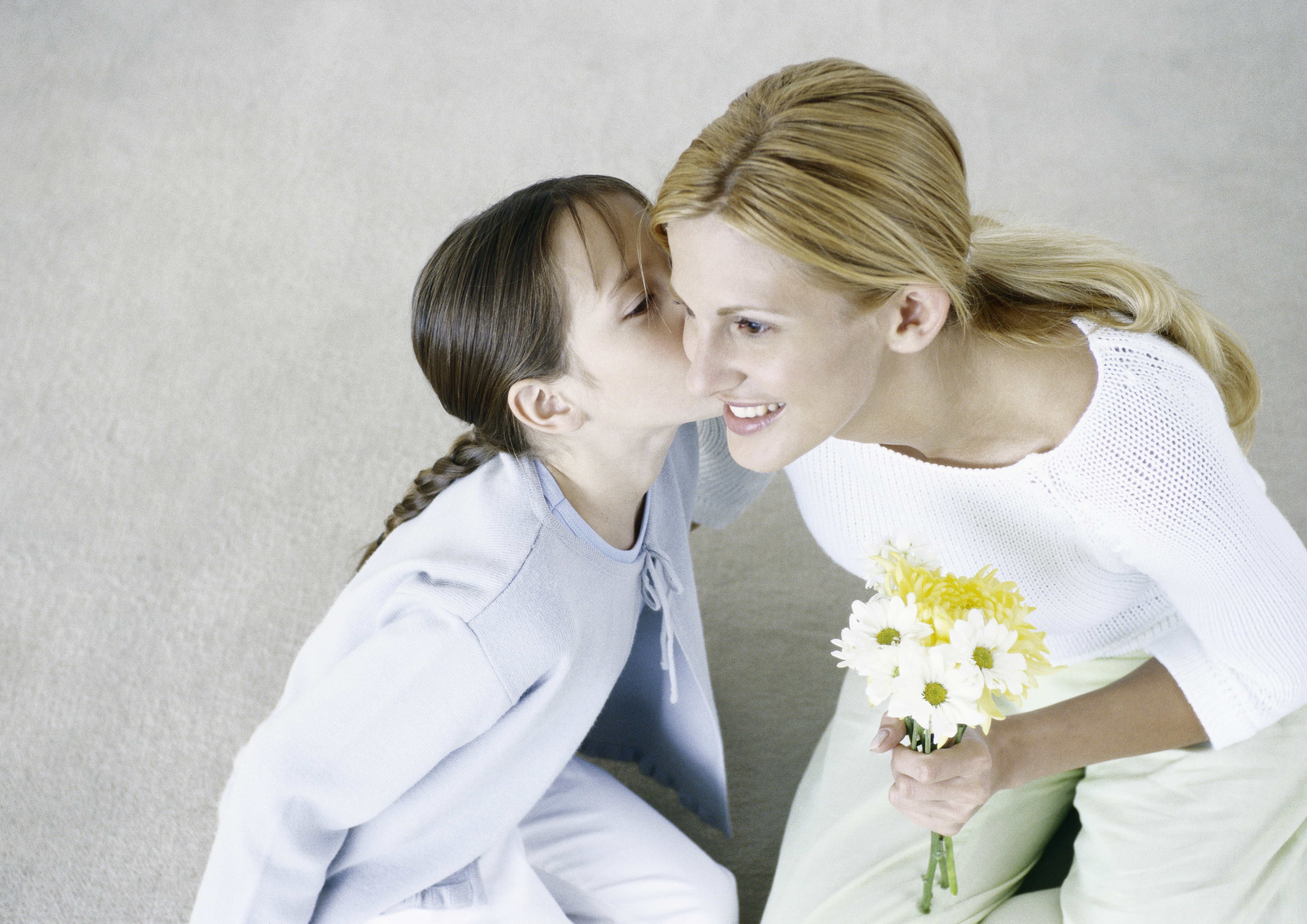 Mujer sosteniendo un ramo de flores, niña besando su mejilla | Foto: Getty Images