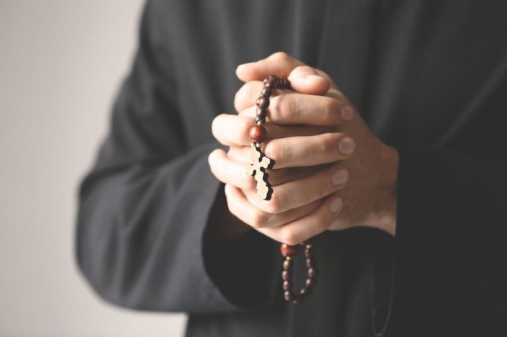 Sacerdote sosteniendo un rosario entre sus puños cerrados. | Imagen: Shutterstock