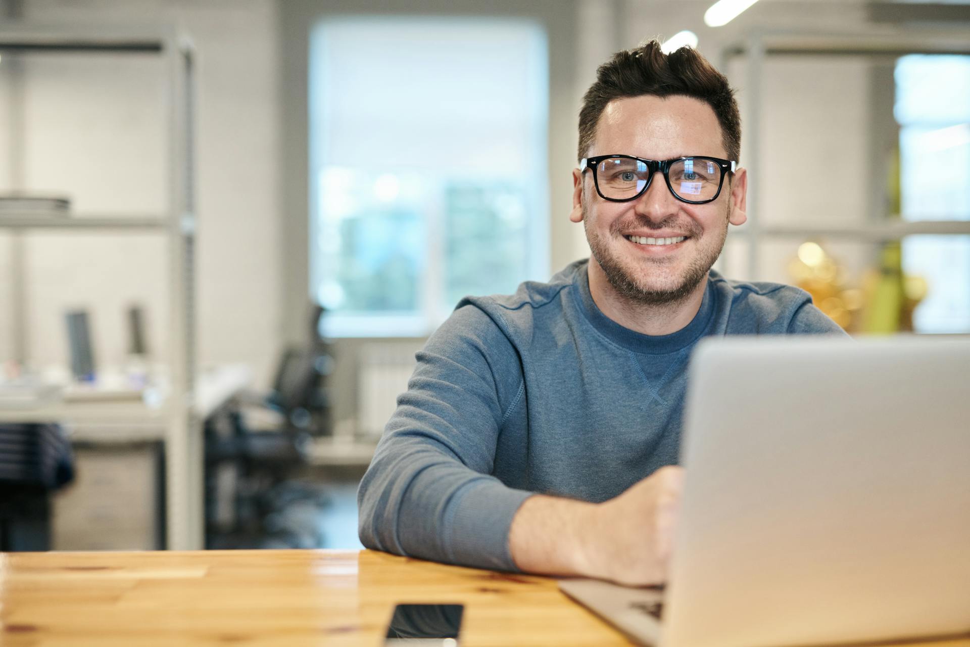 Un hombre sonriente utilizando un portátil en su oficina | Fuente: Pexels