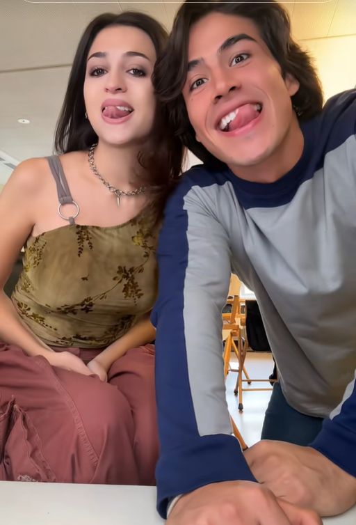Josie Totah y su compañero hacen muecas divertidas a la cámara en otro momento del vídeo de TikTok. Josie lleva la misma camiseta floral de color verde oliva y los mismos pantalones rosas, combinados con un collar de cadena plateada y un bolso bandolera. | Fuente: TikTok/josie totah