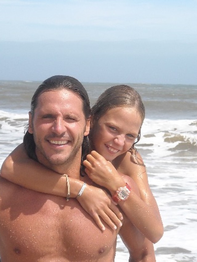 Josefina Bocchino, la hija modelo de Andrea Frigerio y Lucas Bocchino, abrazando a su padre en la playa durante su niñez | Fuente: Instagram/andreafrigeriook