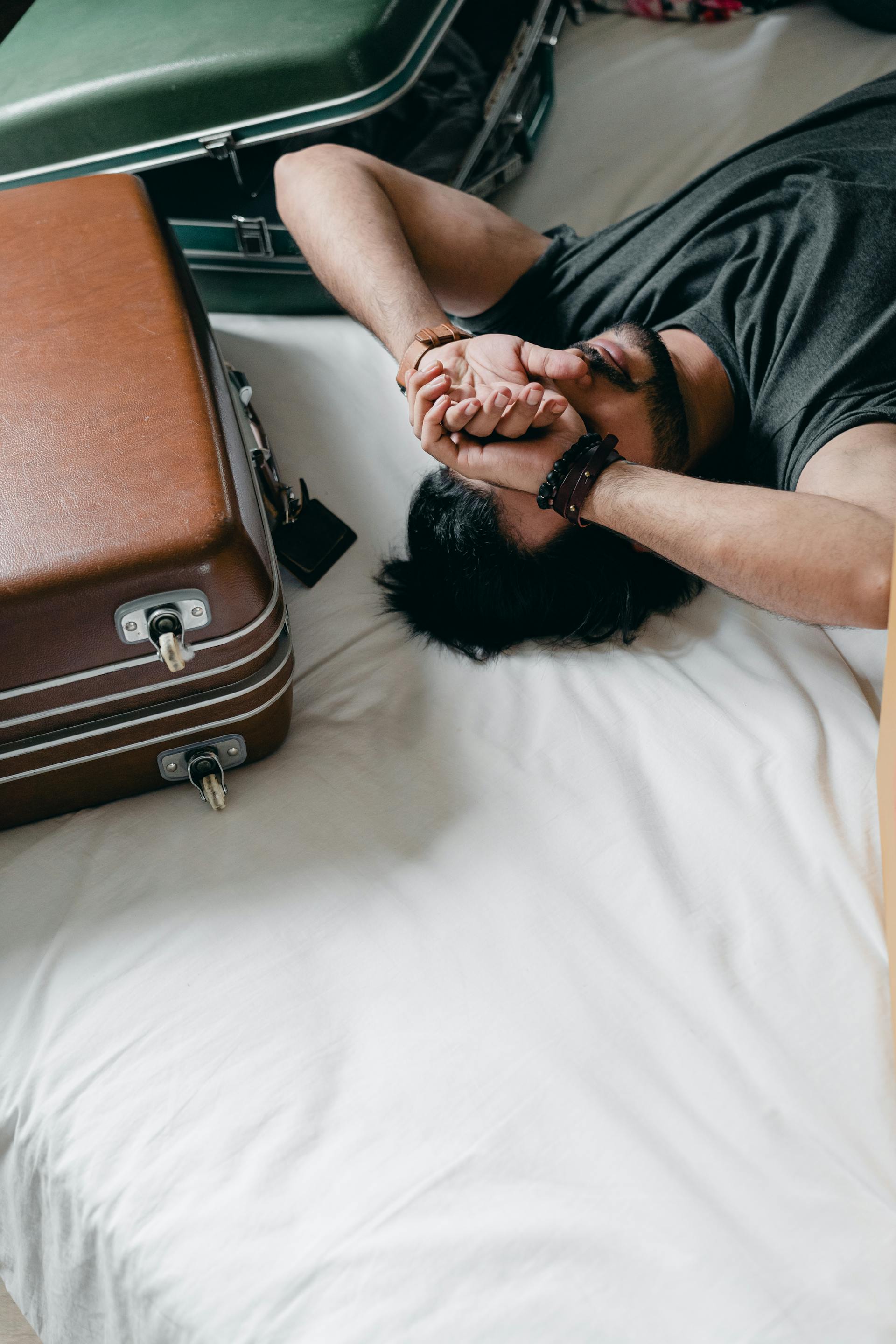 Un hombre cansado tumbado en una cama junto a unas maletas | Fuente: Pexels