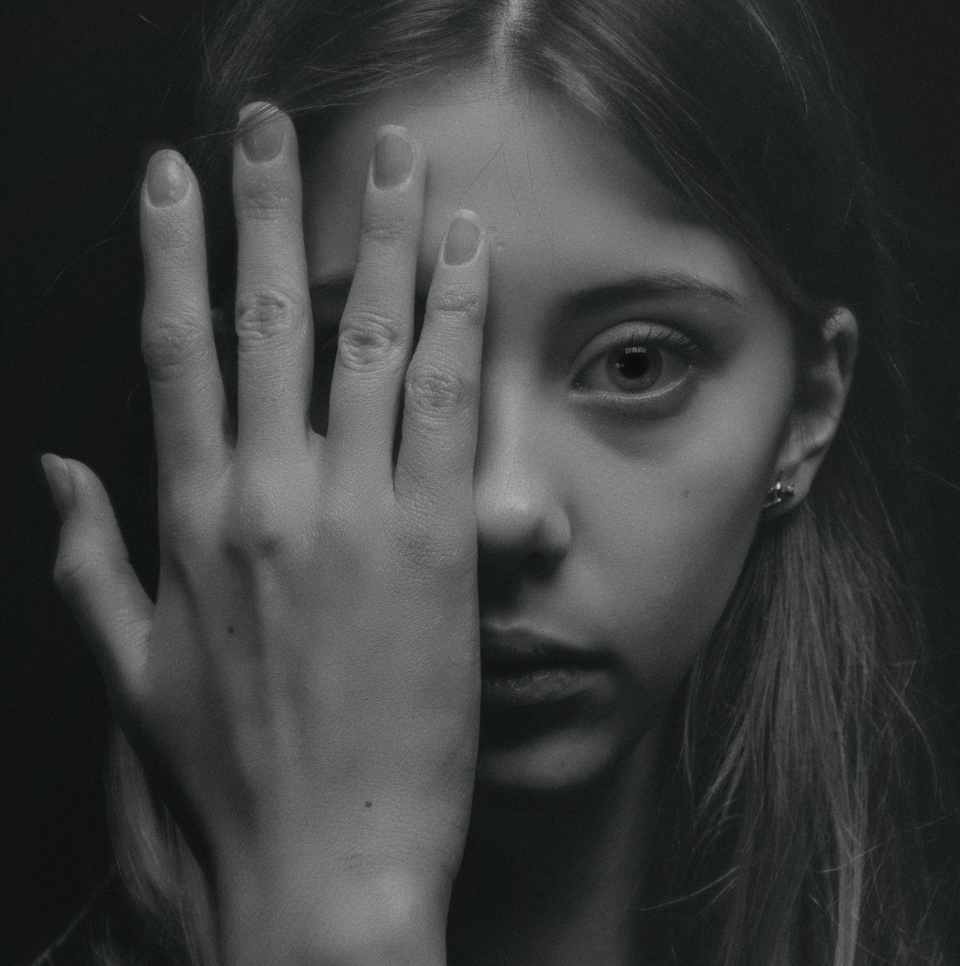 Foto en escala de grises de una mujer cubriéndose la mitad de la cara con la mano | Foto: Pexels