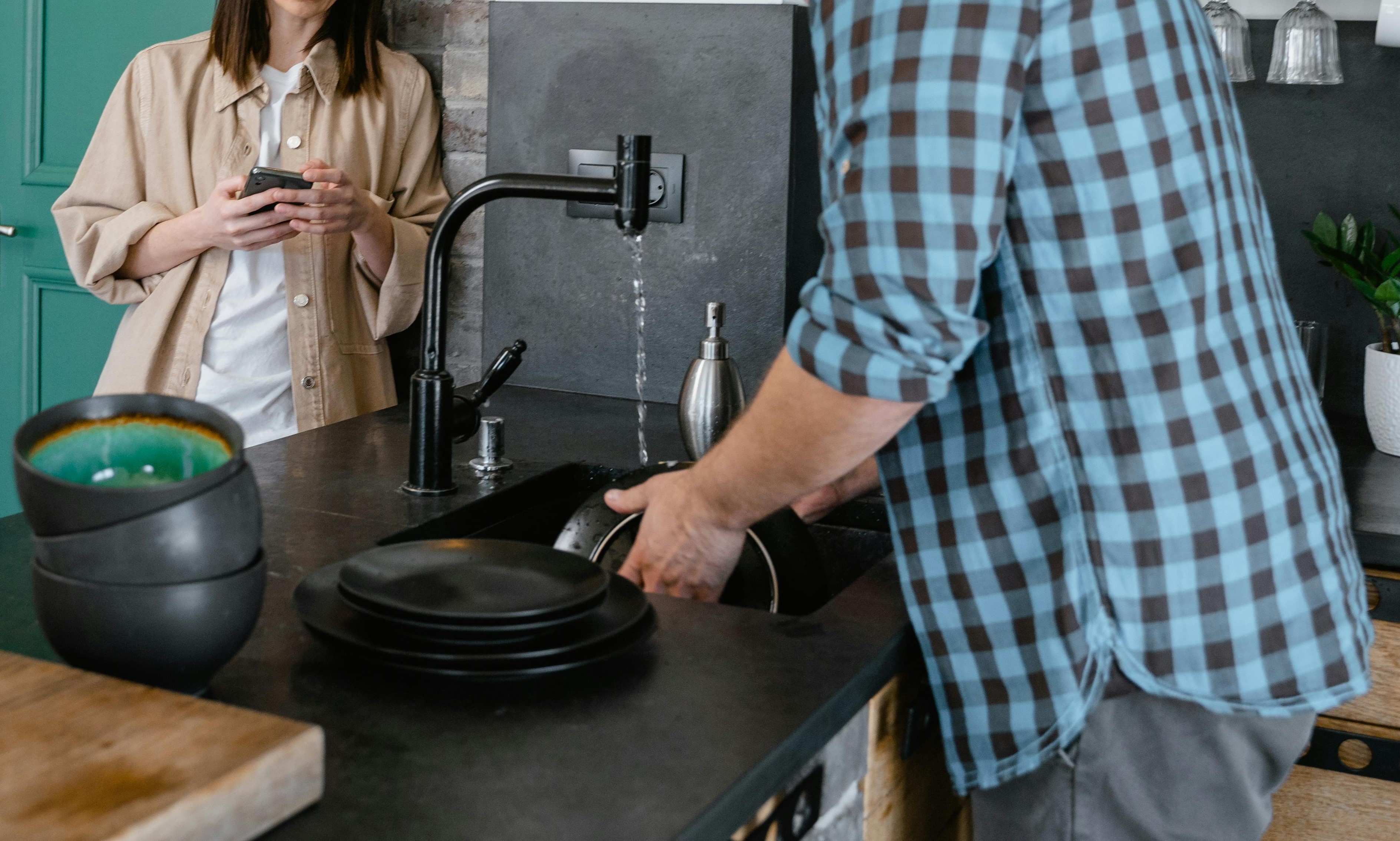 Una mujer observa a un hombre lavando los platos en la cocina | Fuente: Pexels