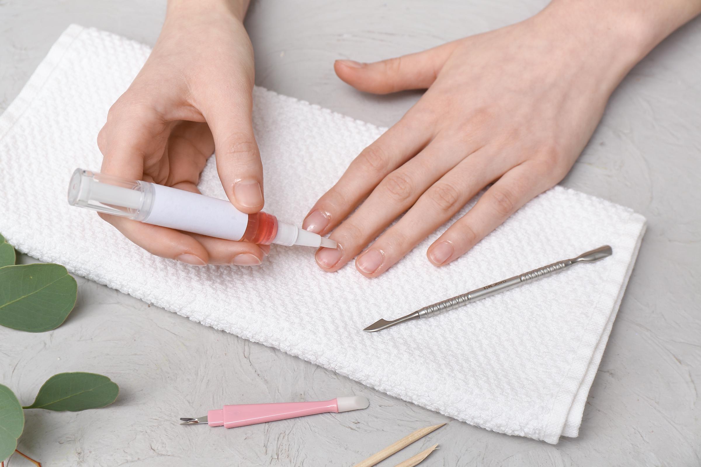 Manos femeninas aplicando aceite para cutículas en las uñas | Fuente: Shutterstock