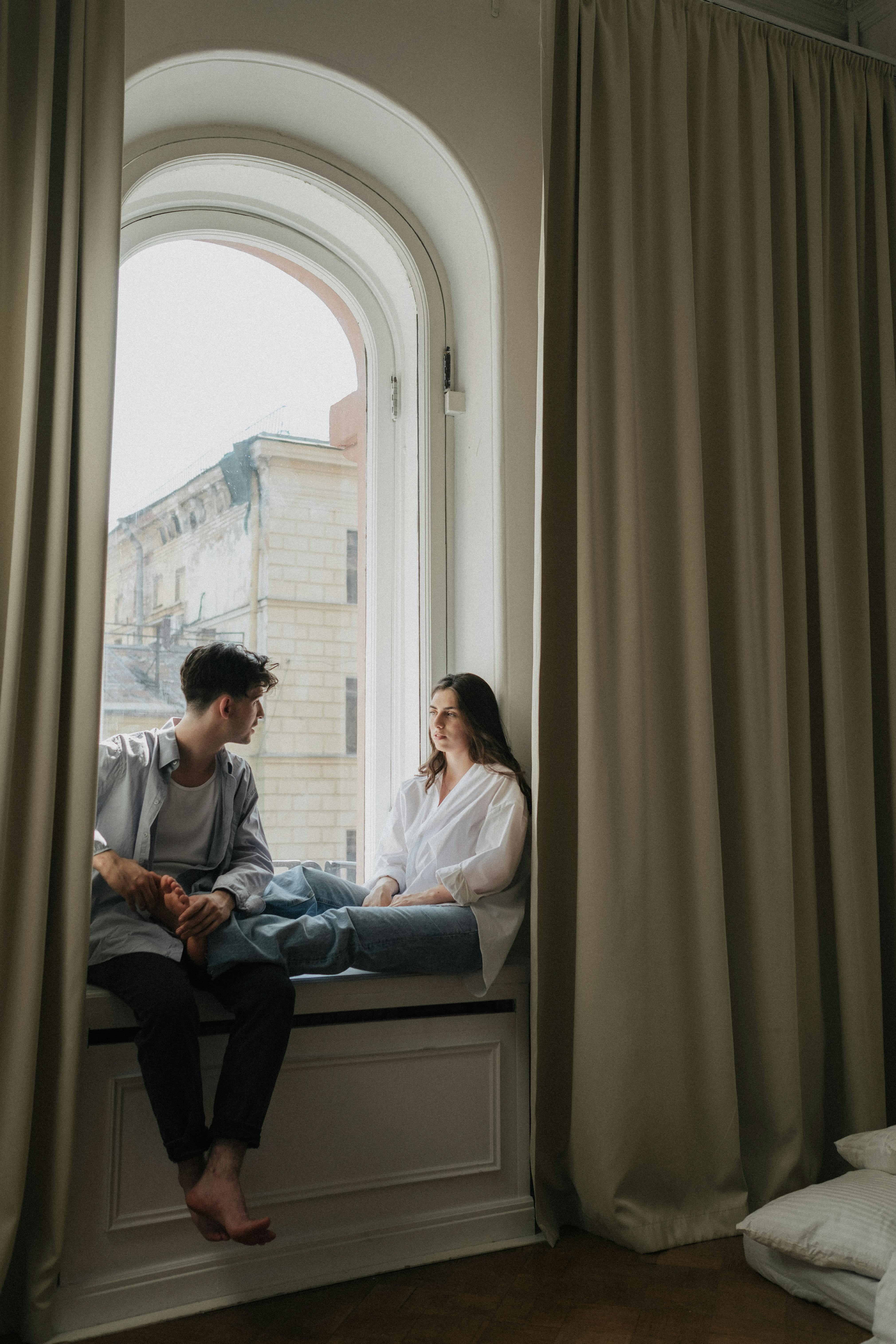 Hombre y mujer sentados en la ventana hablando | Fuente: Pexels