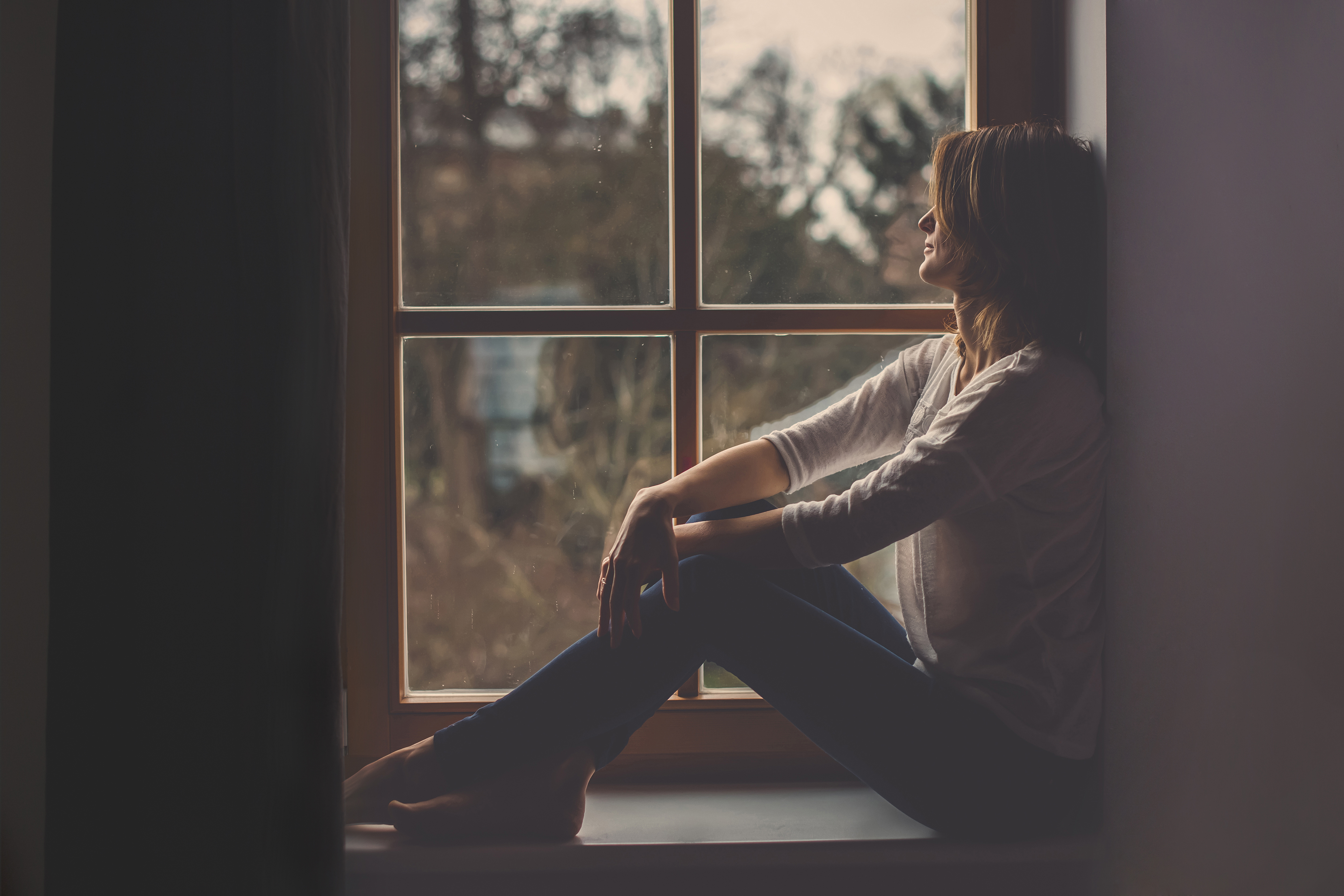 Una mujer sentada junto al alféizar de una ventana mirando al exterior | Foto: Shutterstock