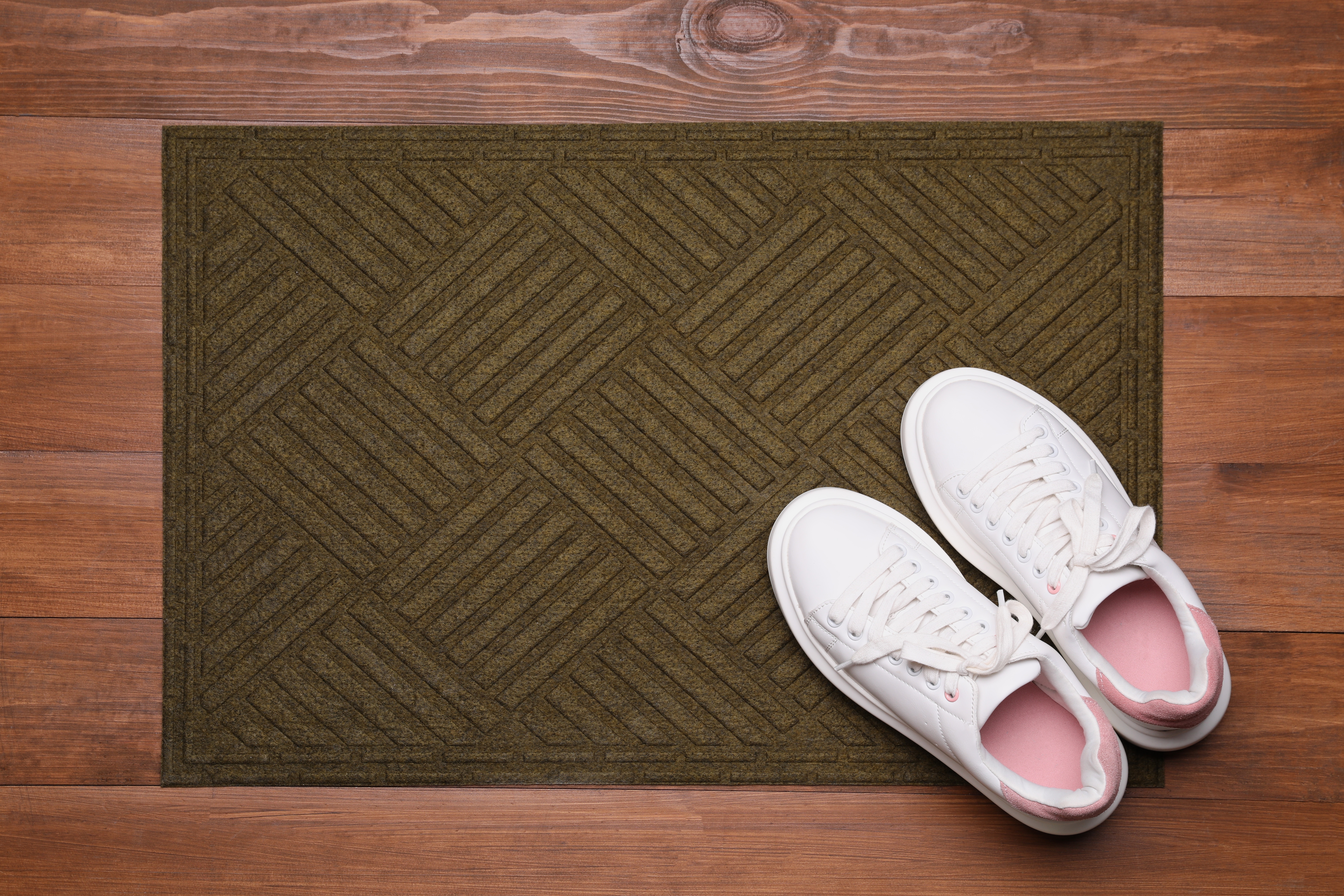 Un par de zapatillas de deporte blancas están colocadas sobre un felpudo tirado en el suelo de madera | Foto: Shutterstock