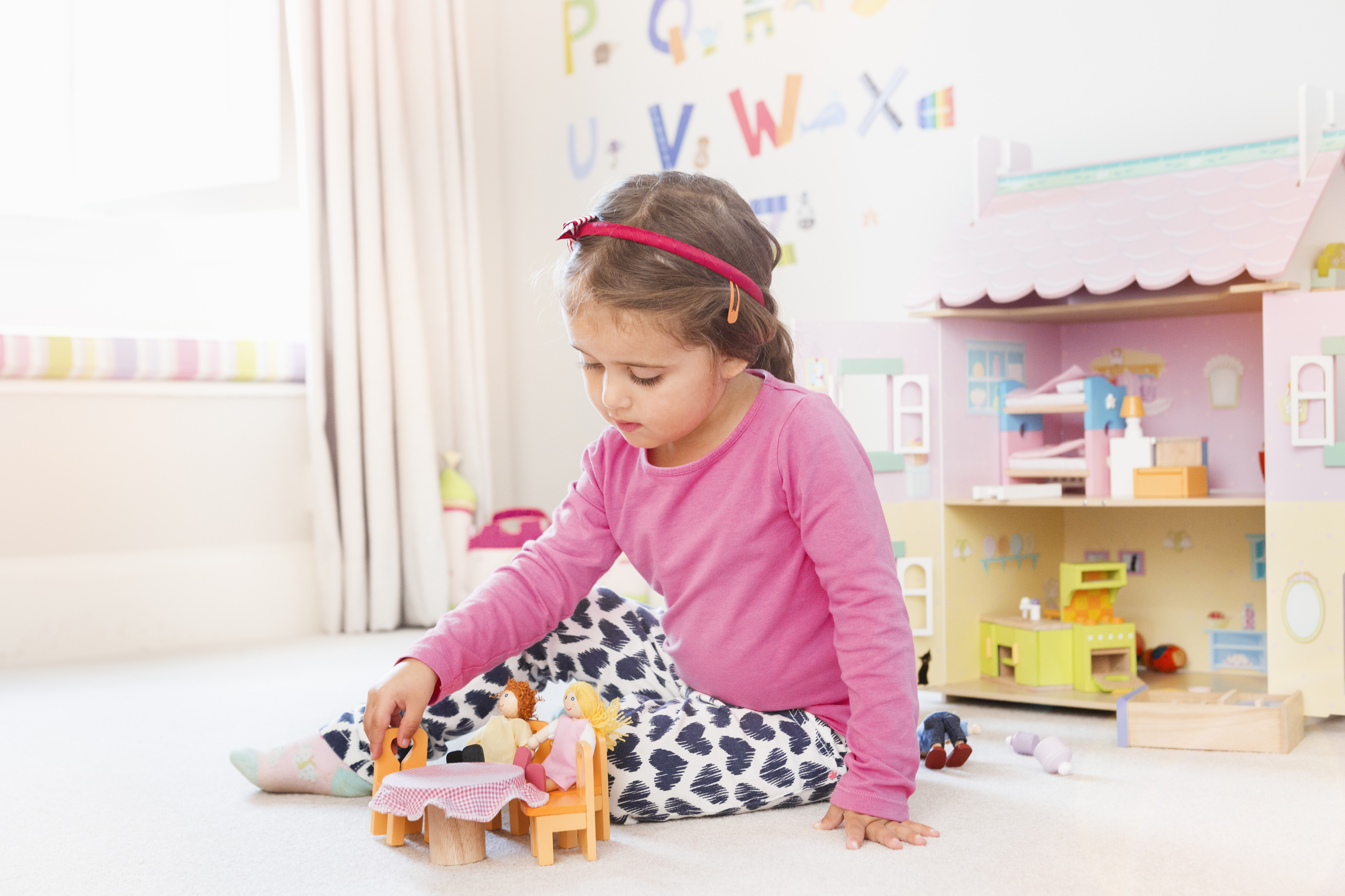 Niña jugando con una casa de muñecas en el dormitorio | Foto: Getty Images