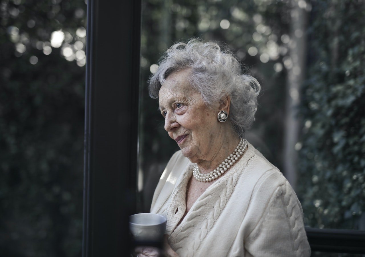 Mujer mayor viendo por una ventana. | Foto: Pexels