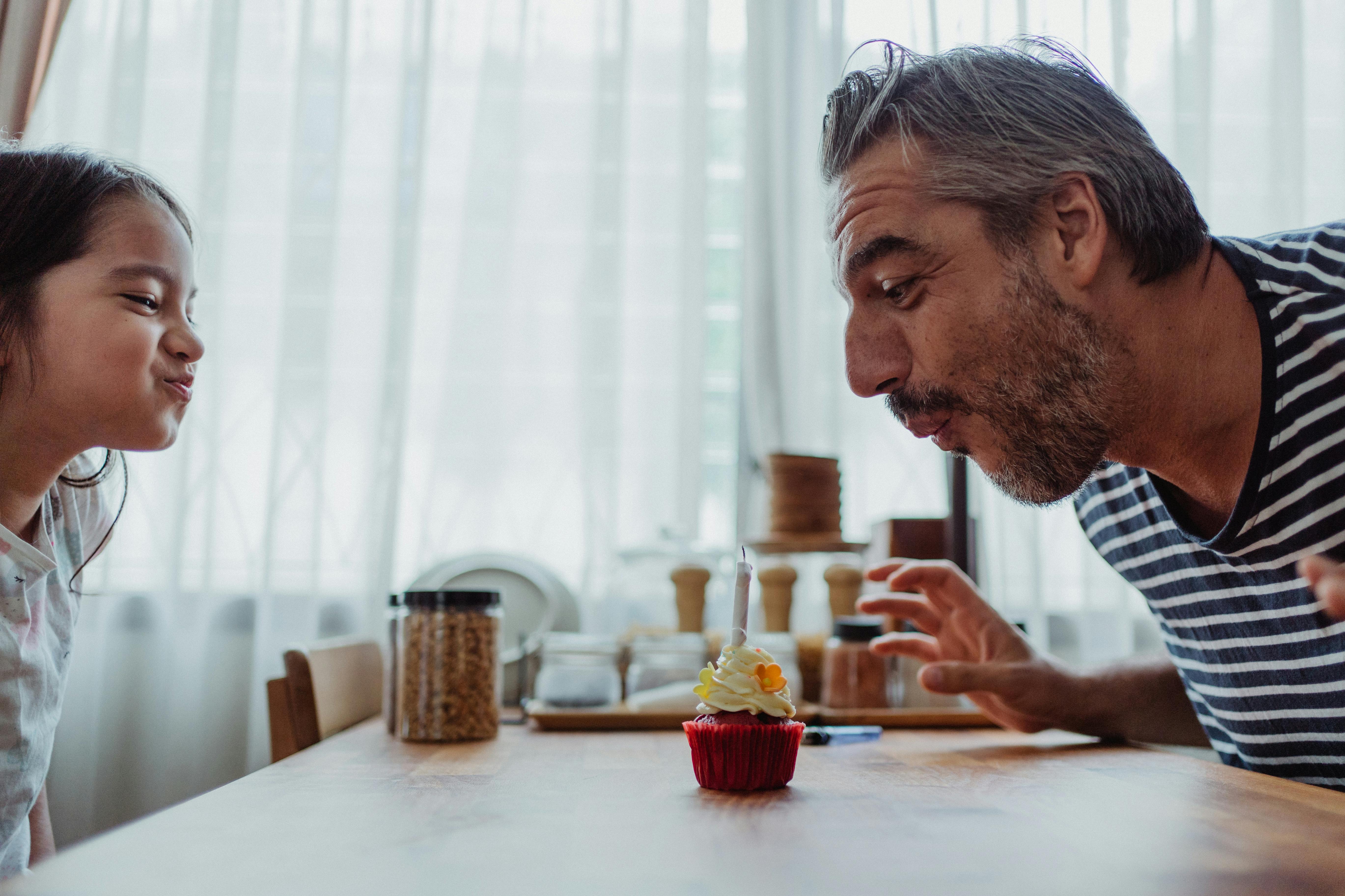 Un hombre y una niña soplando una vela en una magdalena | Fuente: Pexels