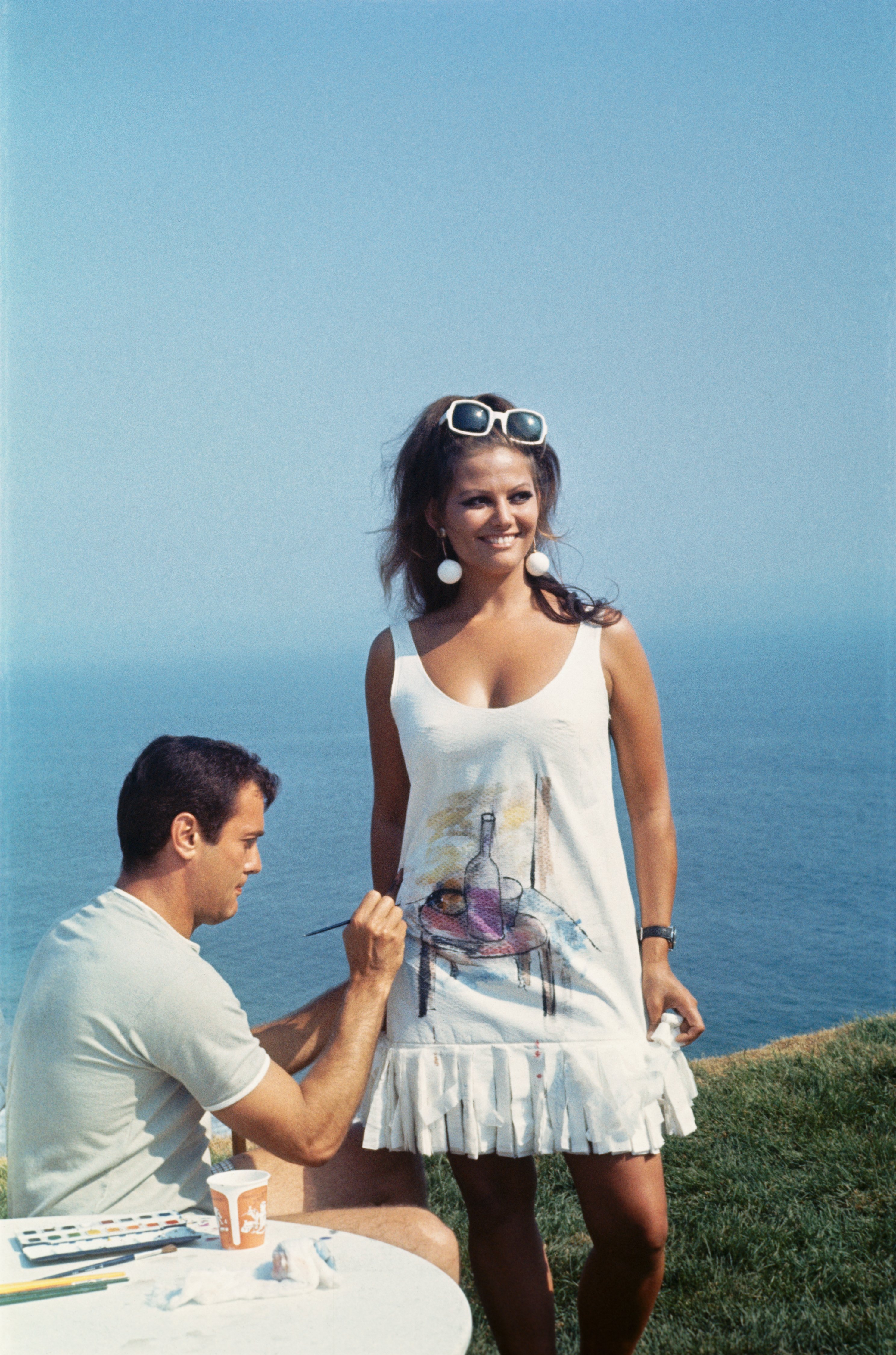 Tony Curtis pinta el vestido de papel de Claudia Cardinale en el set de filmación de la película de 1967, "Don't Make Waves", en California. | Foto: Getty Images