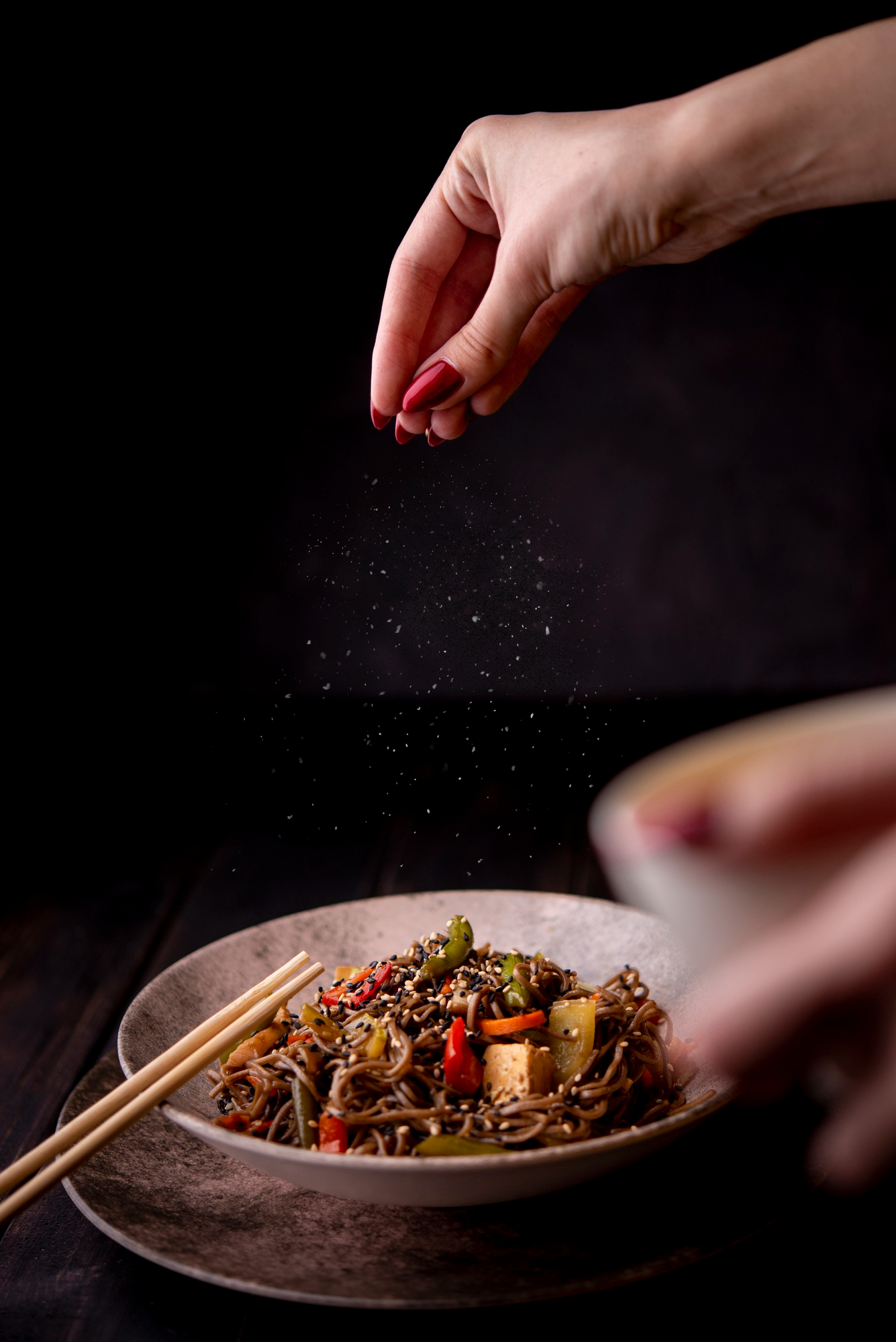 Una mujer espolvoreando sal en un bol de fideos | Fuente: Freepik