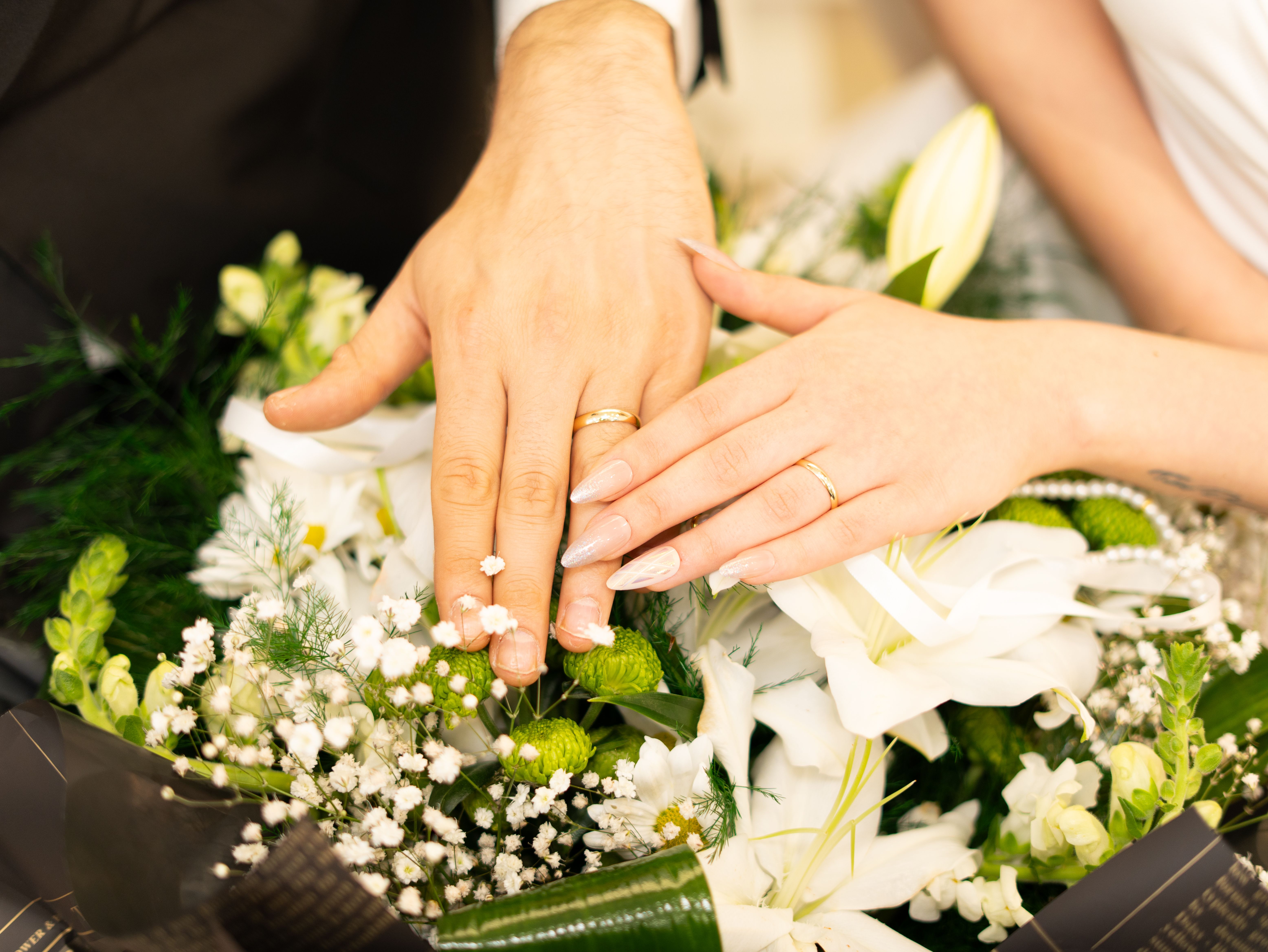 Primer plano de unas manos con anillos de boda apoyadas sobre un ramo de flores | Fuente: Pexels