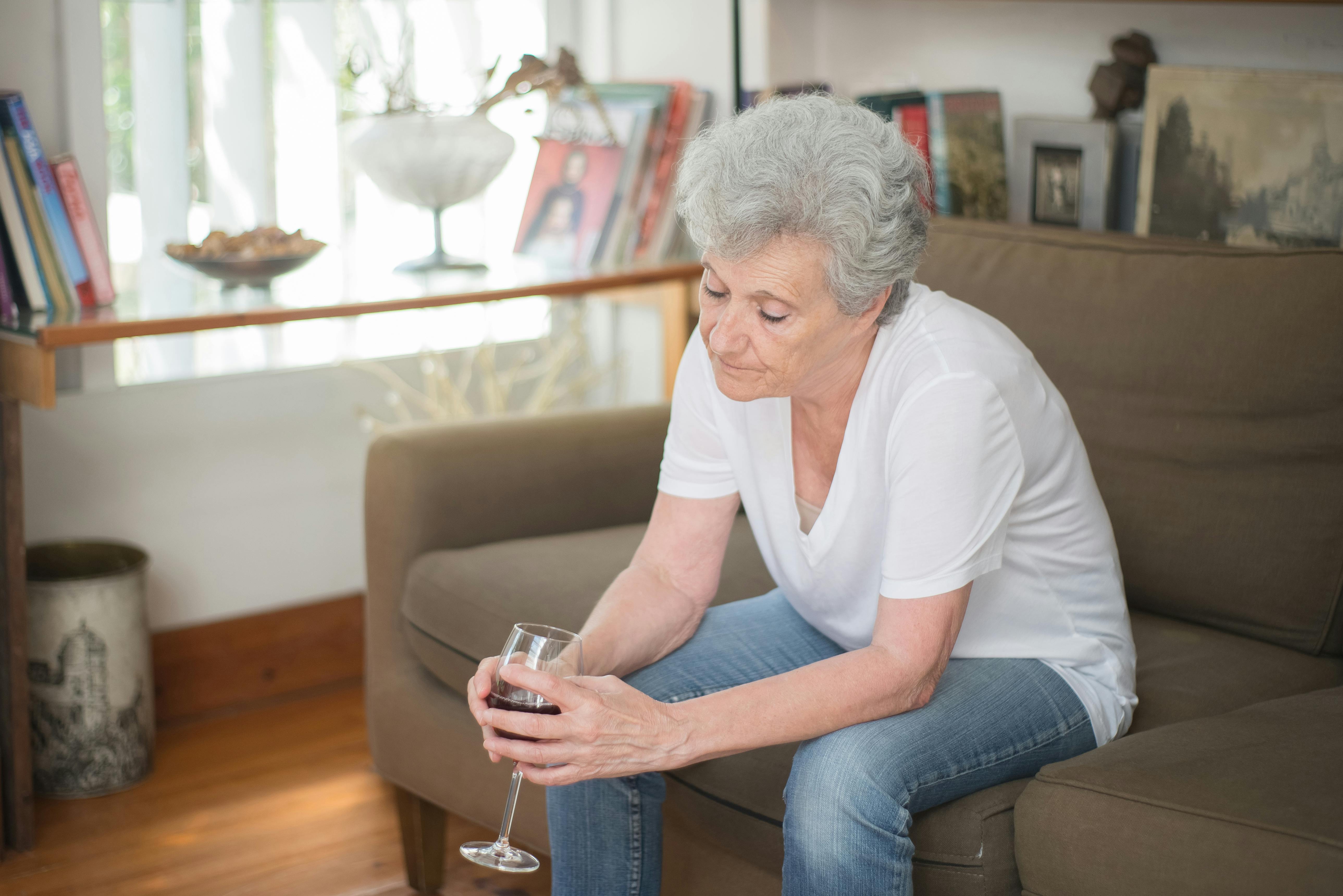 Una mujer de aspecto triste tomando una bebida sentada en un sofá | Fuente: Pexels