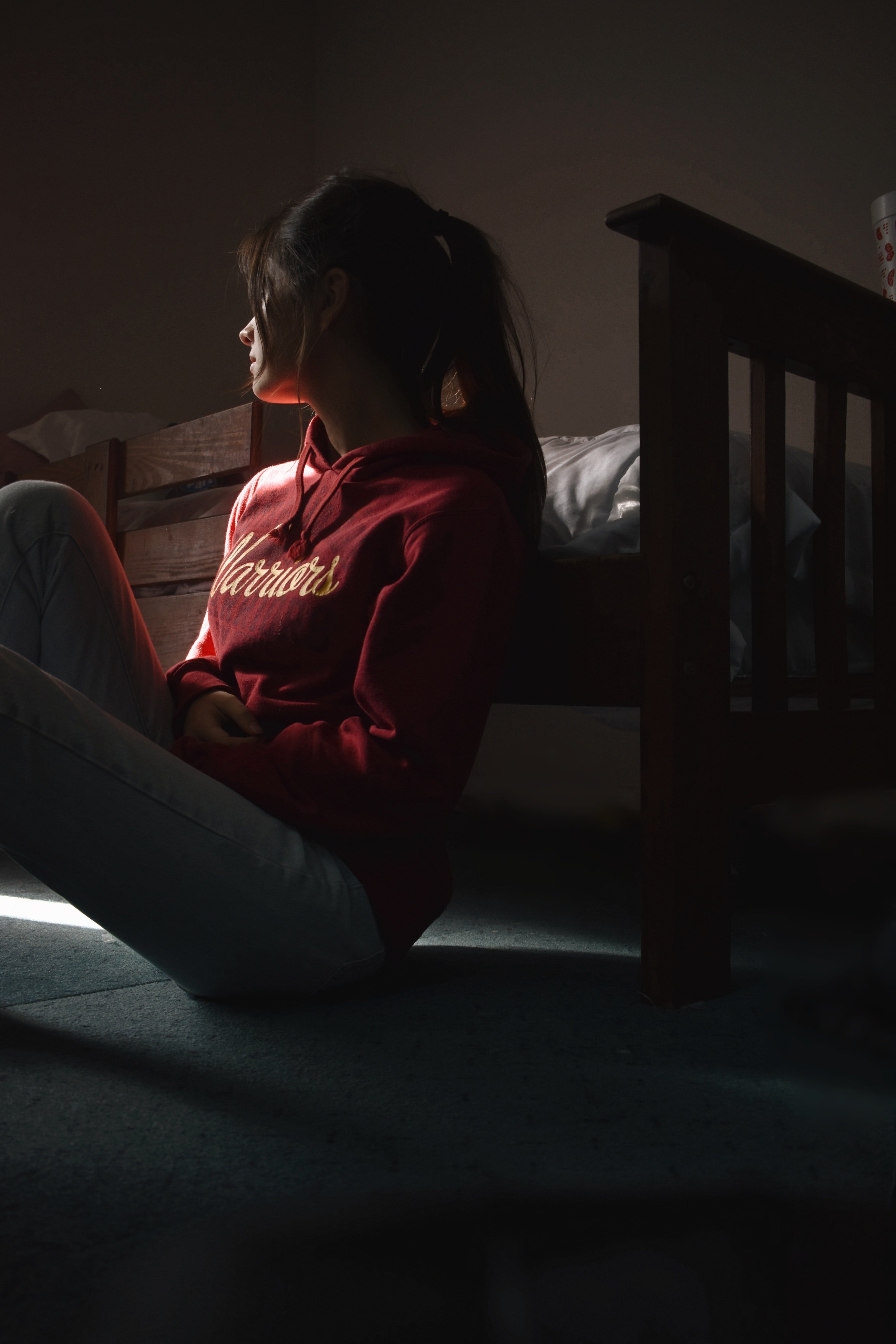 Joven triste sentada en el suelo junto a una cama. | Foto: Pexels