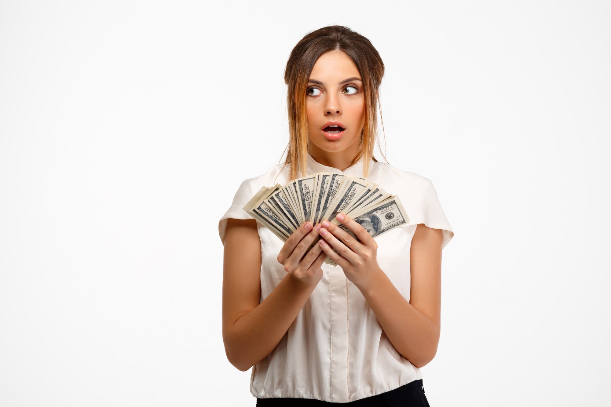 Una mujer joven con cara de sorpresa mientras sostiene dinero | Foto: Freepik