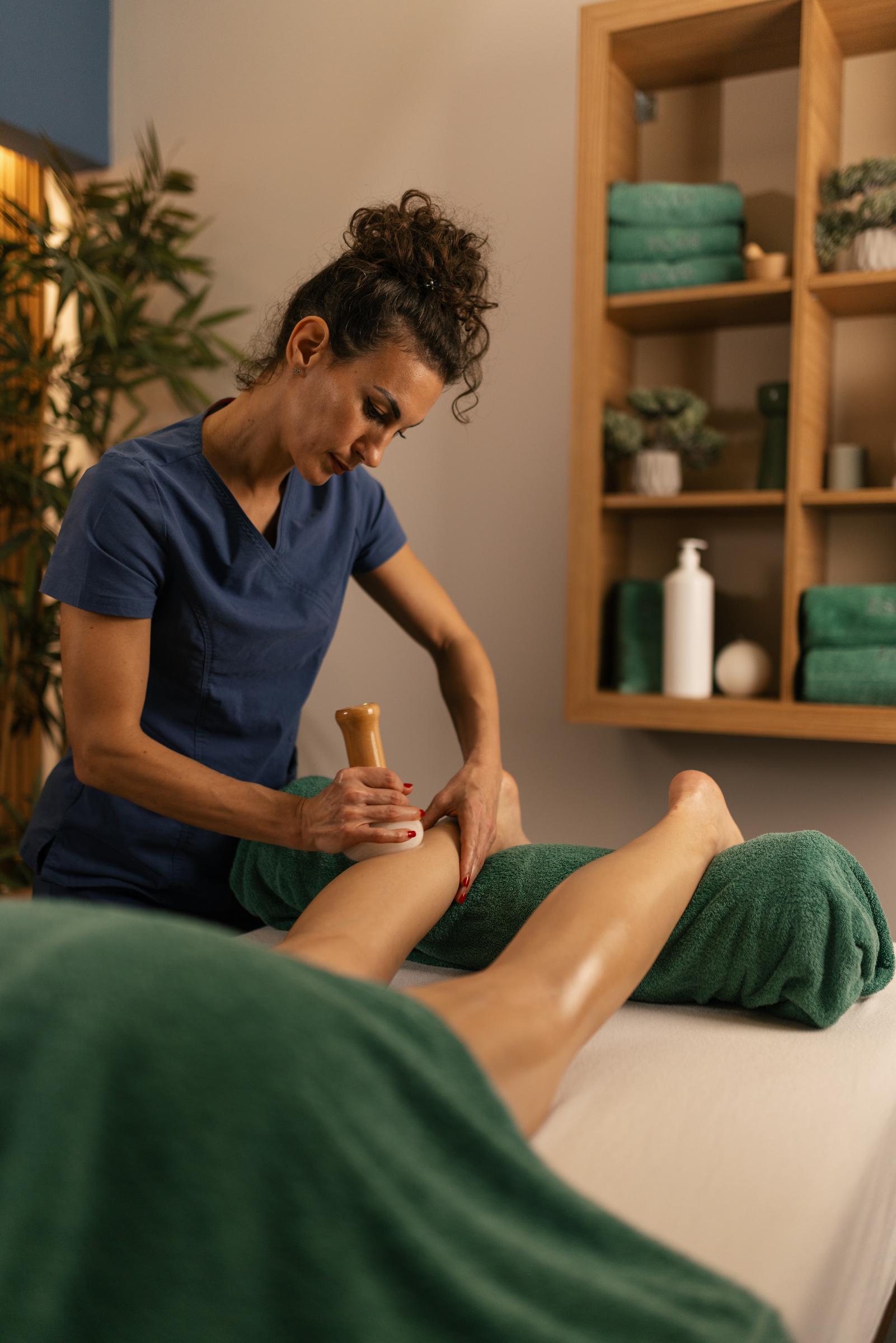 Una mujer aplica un masaje Gua Sha en las piernas de un cliente | Fuente: Getty Images
