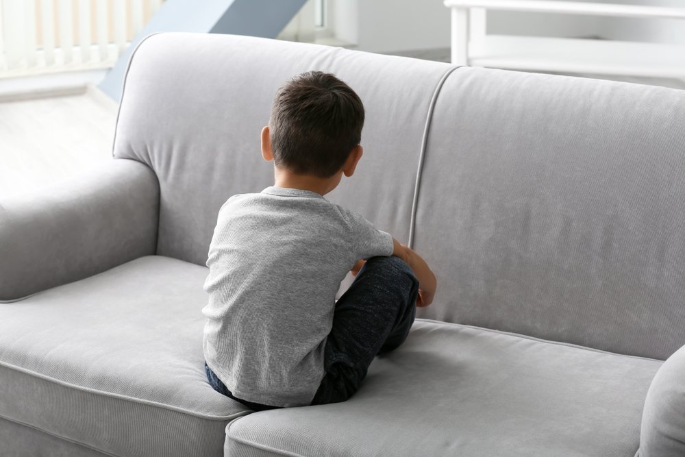 Niño afligido sentado en un sofá de cara al espaldar. | Foto: Shutterstock