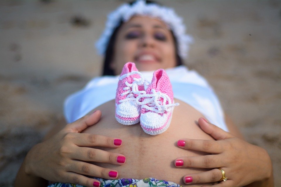 Mujer embarazada recostada con zapatitos sobre su panza. | Imagen: Max Pixel