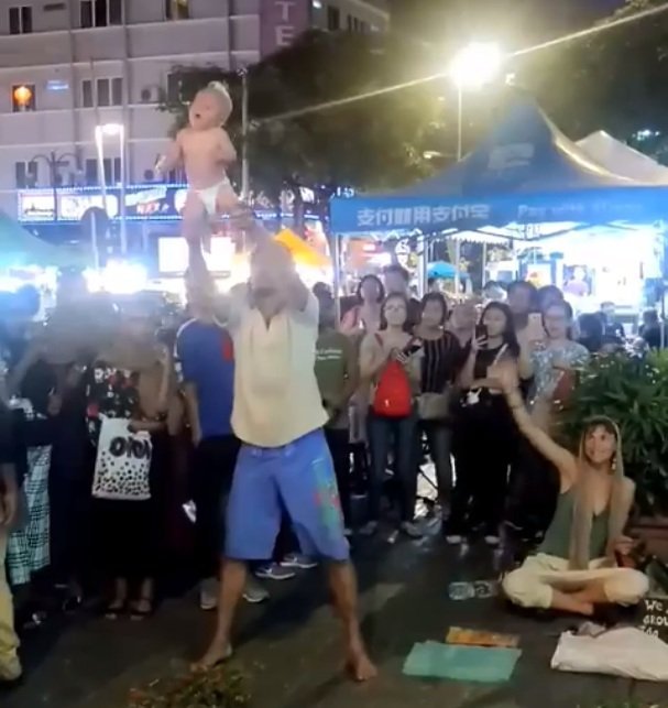 Un padre lanza a su bebé en el aire por las piernas durante un espectáculo callejero en Kuala Lumpur. / Foto: Facebook / Zayl Chia Abdulla