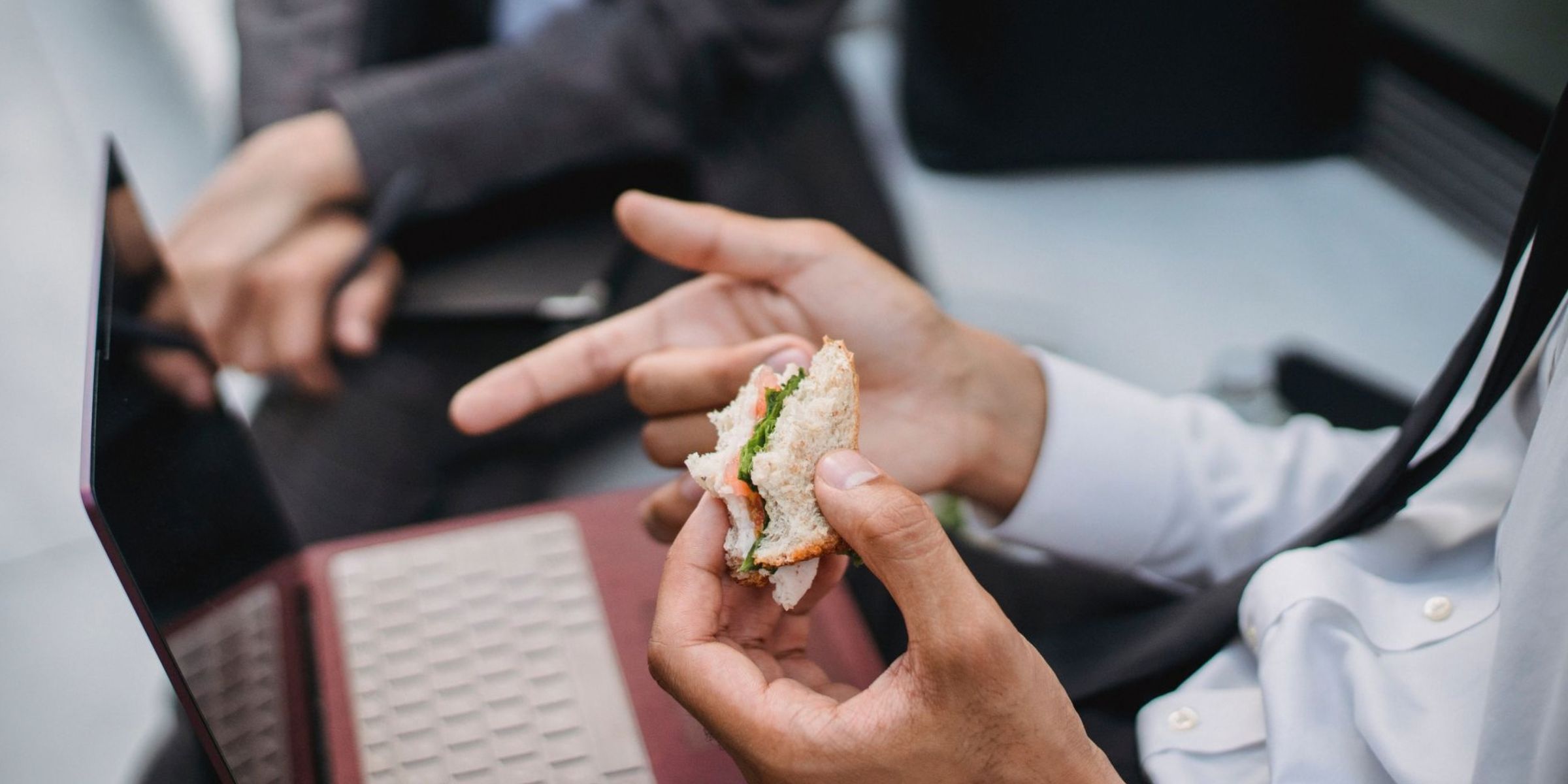 Un hombre comiéndose un bocadillo mientras trabaja con el portátil | Fuente: Pexels