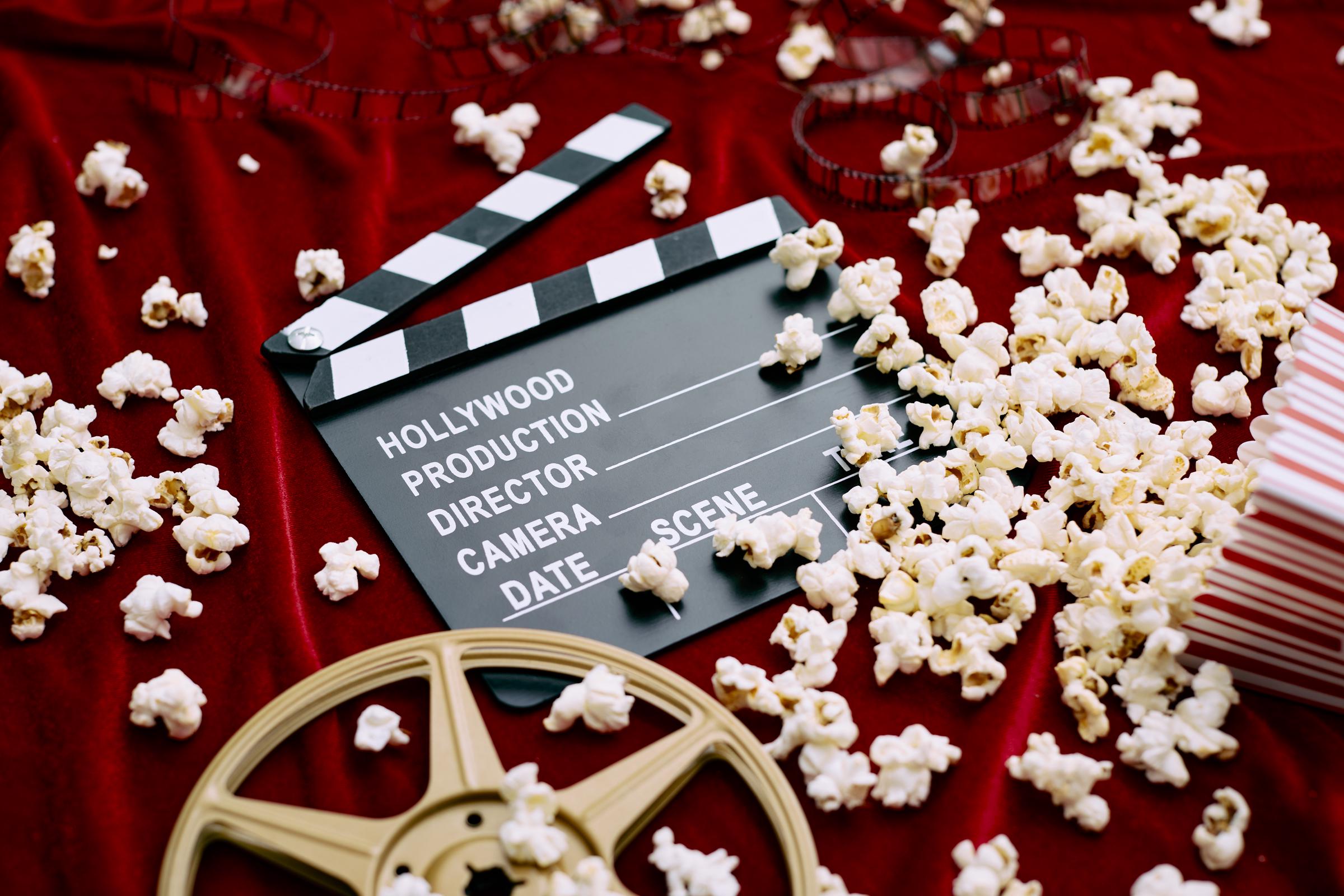 Una claqueta, un carrete de película, una película y palomitas derramadas sobre un fondo de satén rojo | Fuente: Getty Images