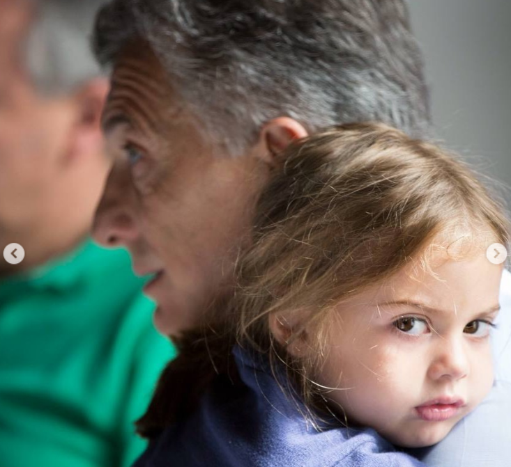 Antonia descansa en brazos de su padre con un gesto pensativo y nostálgico. Con su cabello castaño claro ligeramente desordenado y una prenda azul, la niña apoya su mejilla sobre el hombro de Mauricio Macri, quien aparece de perfil con semblante sereno. | Fuente: Instagram/mauriciomacri