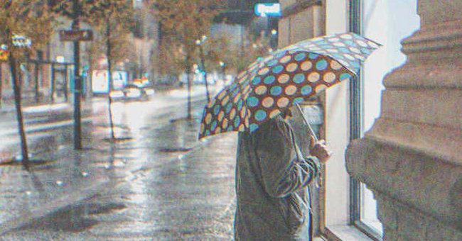 Una anciana con un paraguas en la mano y mirando el interior de un negocio | Foto: Shutterstock